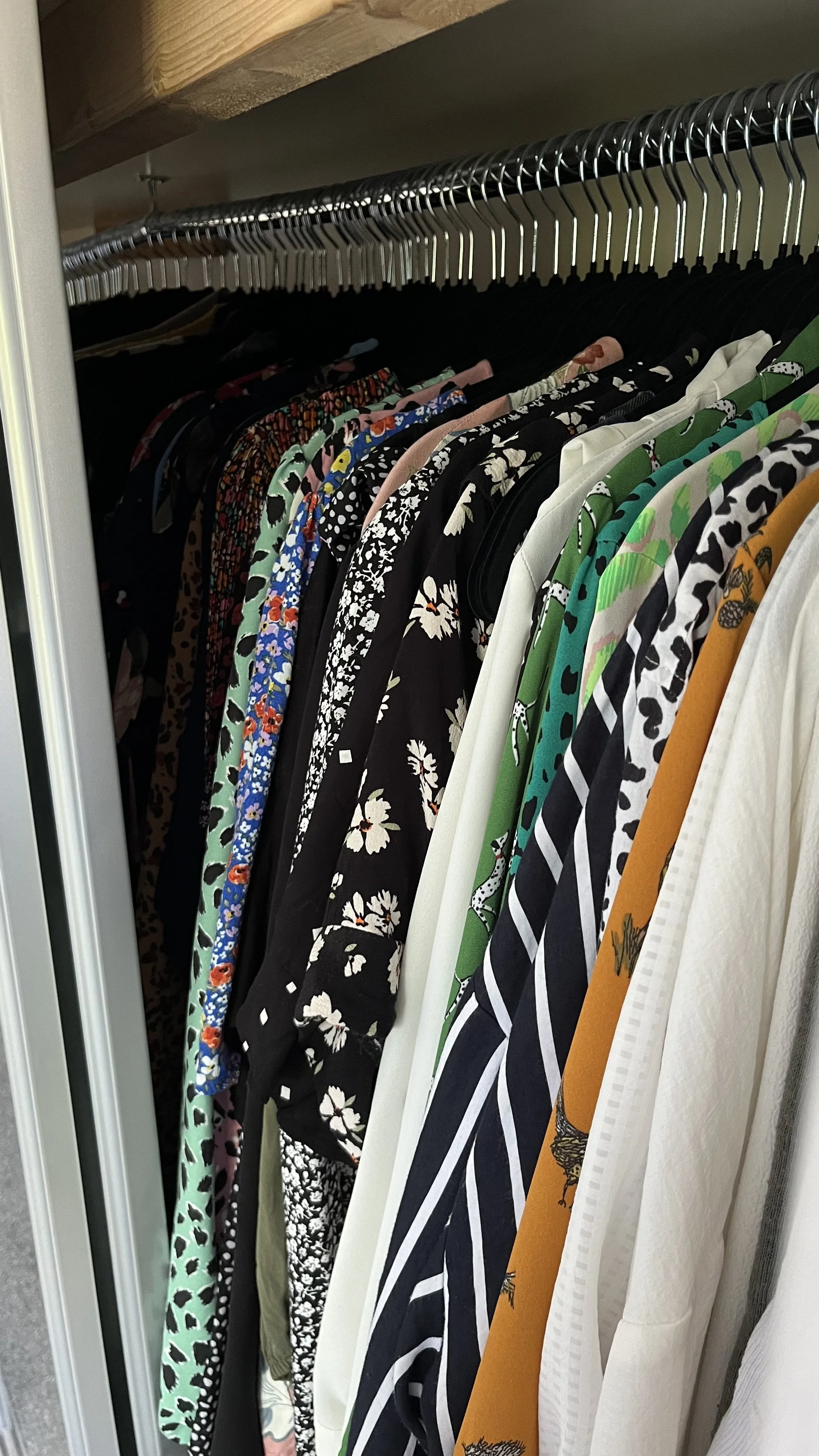 Clothes hanging in a closet, with various patterns and colors including floral, animal print, and stripes.