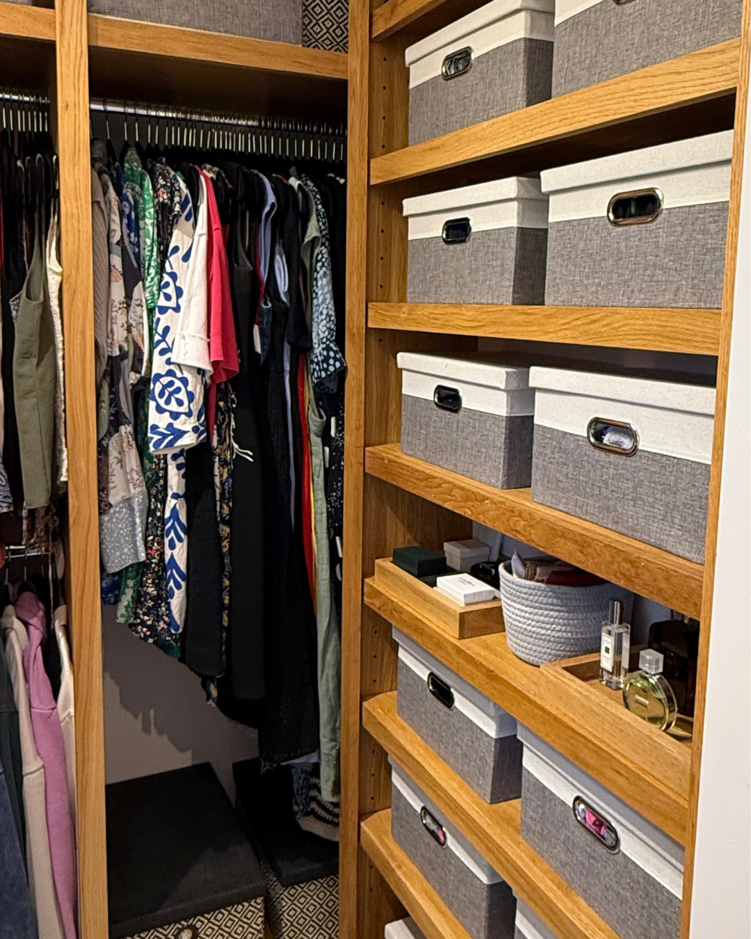 Clothes hanging in a closet with organised storage boxes on wooden shelves.