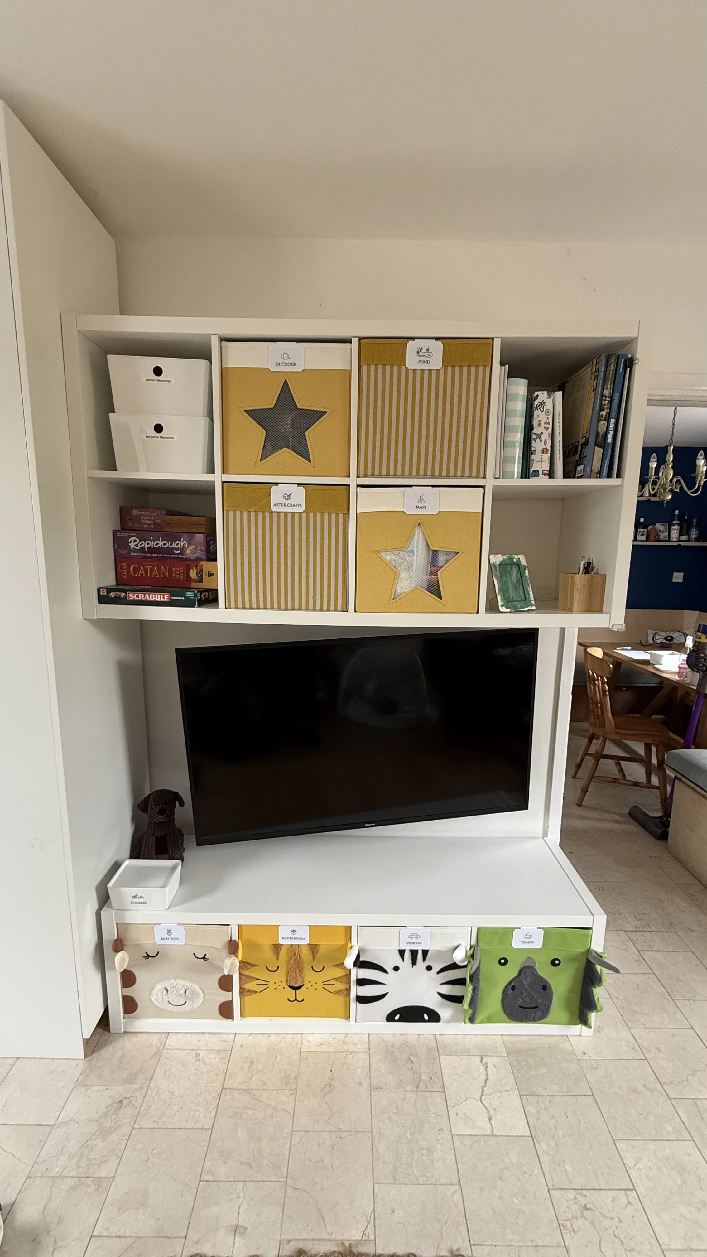 Living room entertainment center with a flat screen TV, decorative storage baskets featuring animal faces, and shelves with books and games.