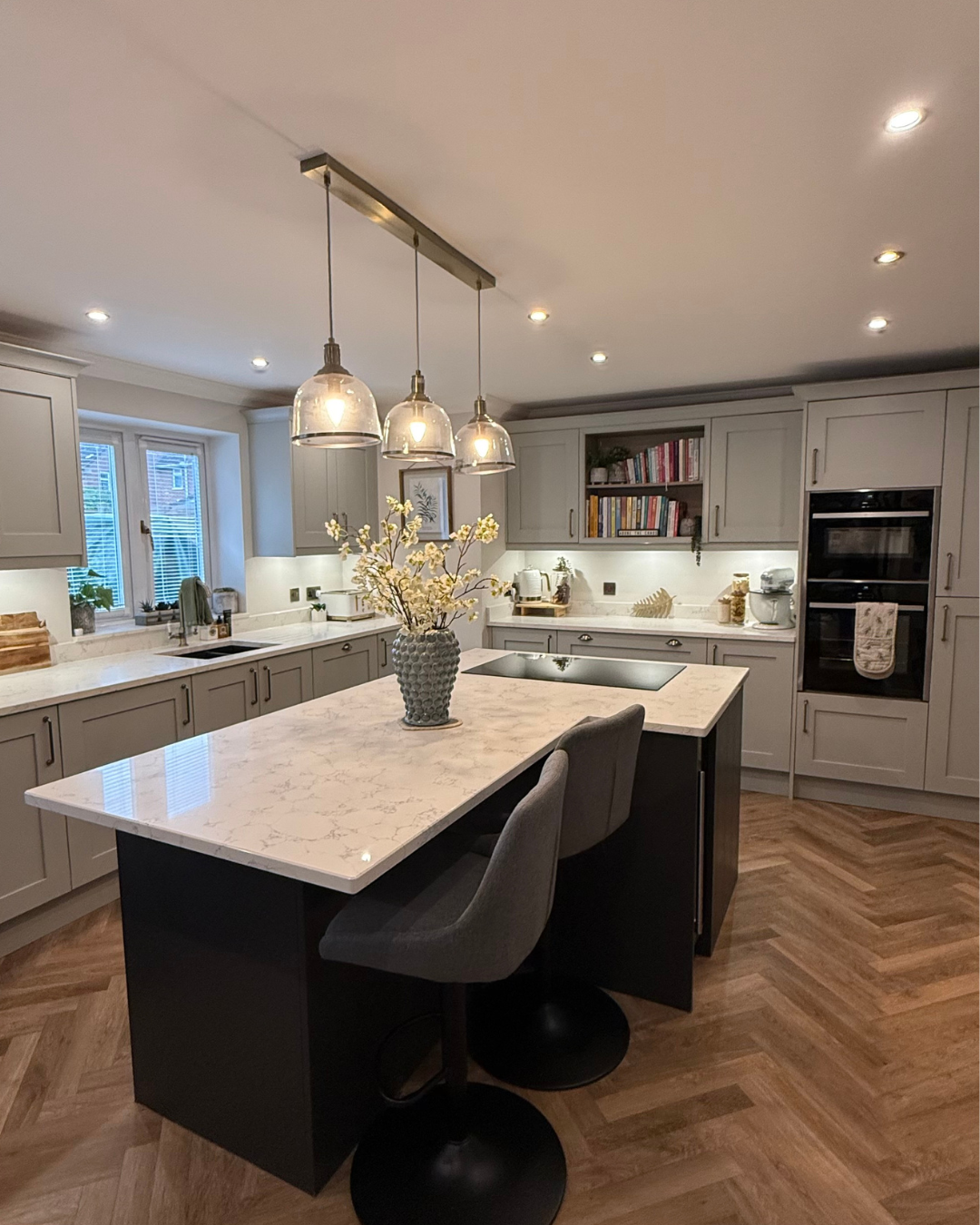 Modern kitchen with gray cabinetry, white marble countertops, a kitchen island with bar stools, hanging pendant lights, and hardwood flooring.