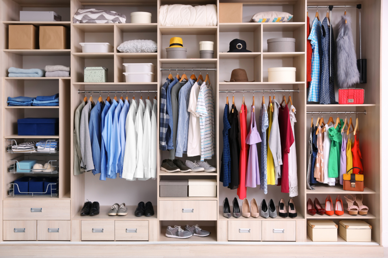 Organized closet with shelves of folded clothes, shoes, hats, storage boxes, and hanging garments.