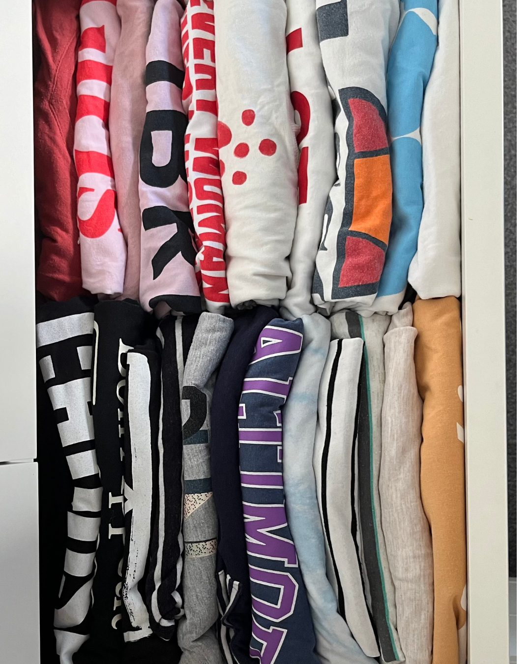 Stacked colorful folded sweatshirts or T-shirts with various patterns and logos.
