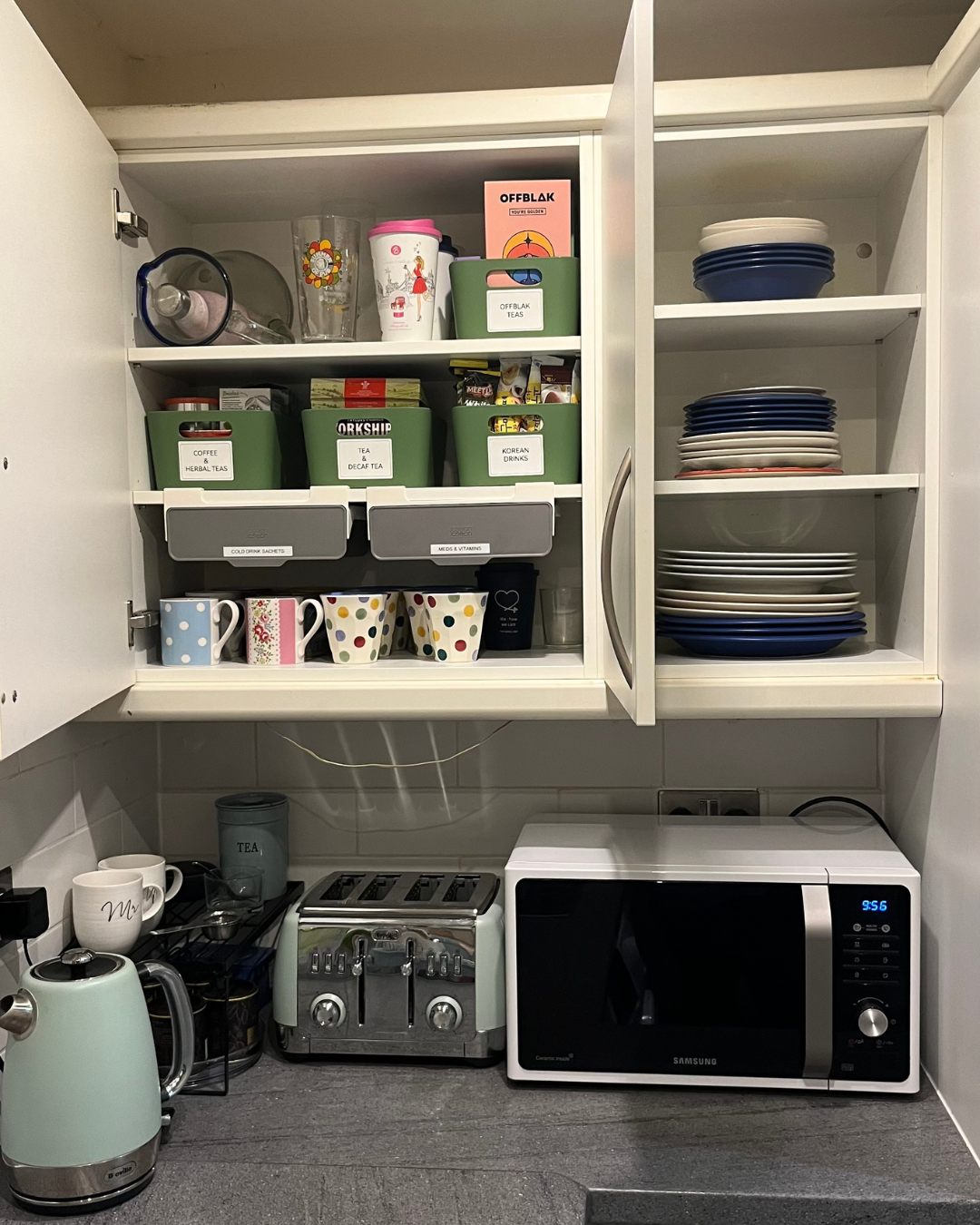 Kitchen cabinet with plates, bowls, cups, glasses, tea and coffee supplies, a toaster, and a microwave on the countertop.