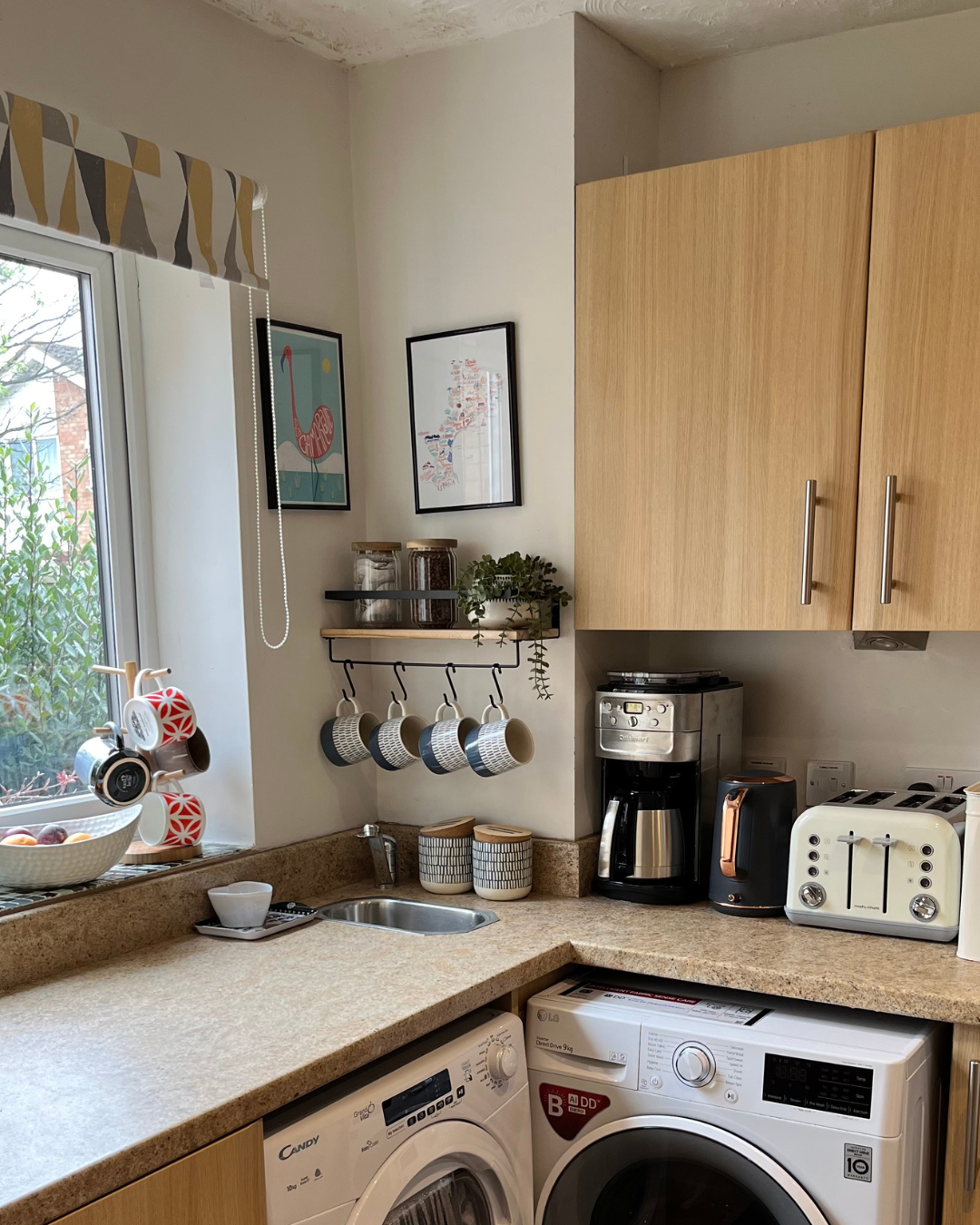 Kitchen with a window, hanging cups, coffee machine, toaster, laundry washer and dryer, and wall art.