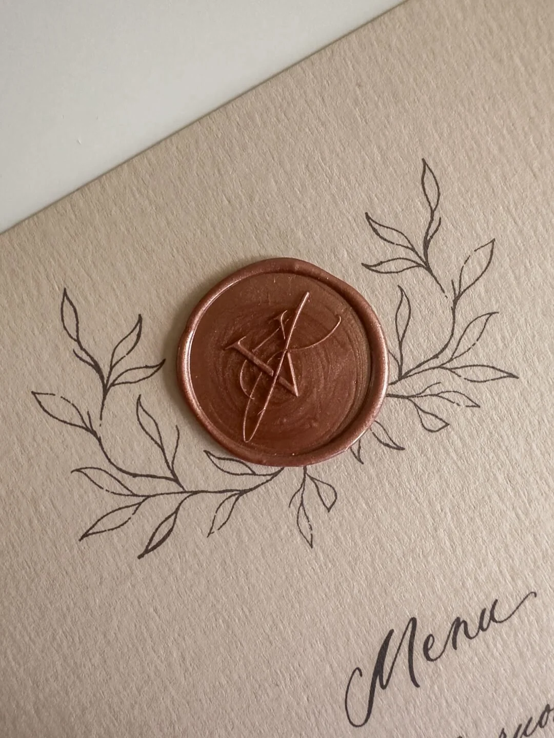 Häiden menun yksityiskohtana ruskea sinetti hääparin erukirjaimista muodostetulla monogrammilla ja kranssikuviolla.