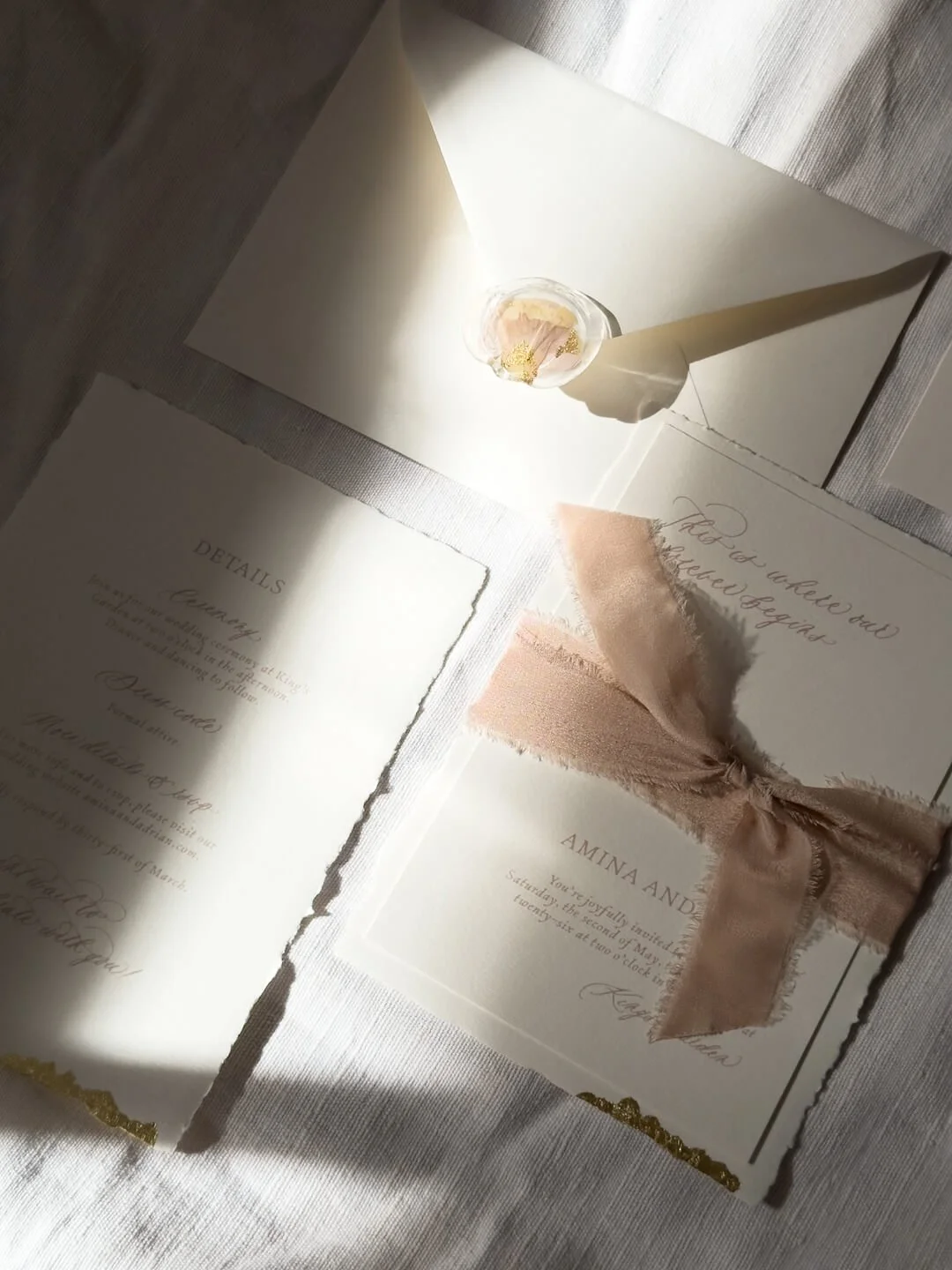 Romanttiset hääkutsut, joissa vaaleanpunainen silkkinauha, lehtikultaa, revityt reunat ja kukkasinetti.