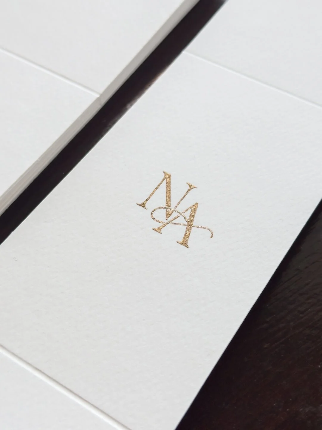 Elegantti kultainen monogrammi hääkutsun vyötteessä.