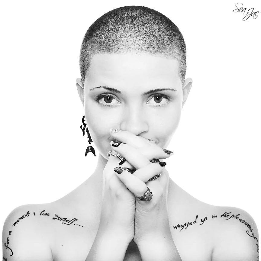 woman with shaved head shoulder tattoos piercing gaze symmetrical portrait