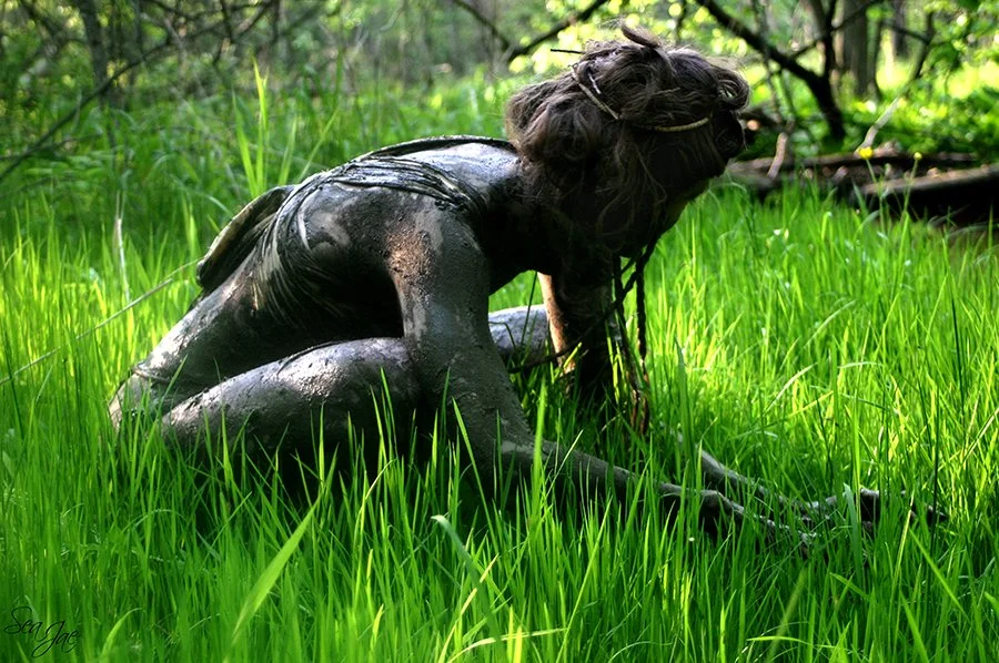 tribal woman covered in mud crouching in tall grass