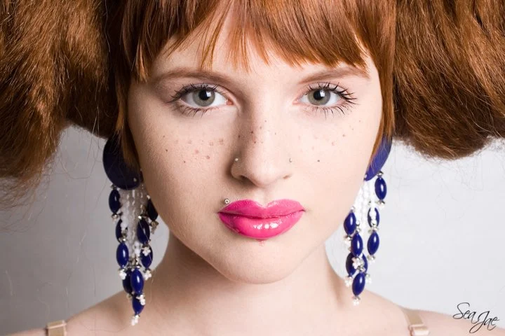 redheaded woman pink lips big blue earrings fake freckles