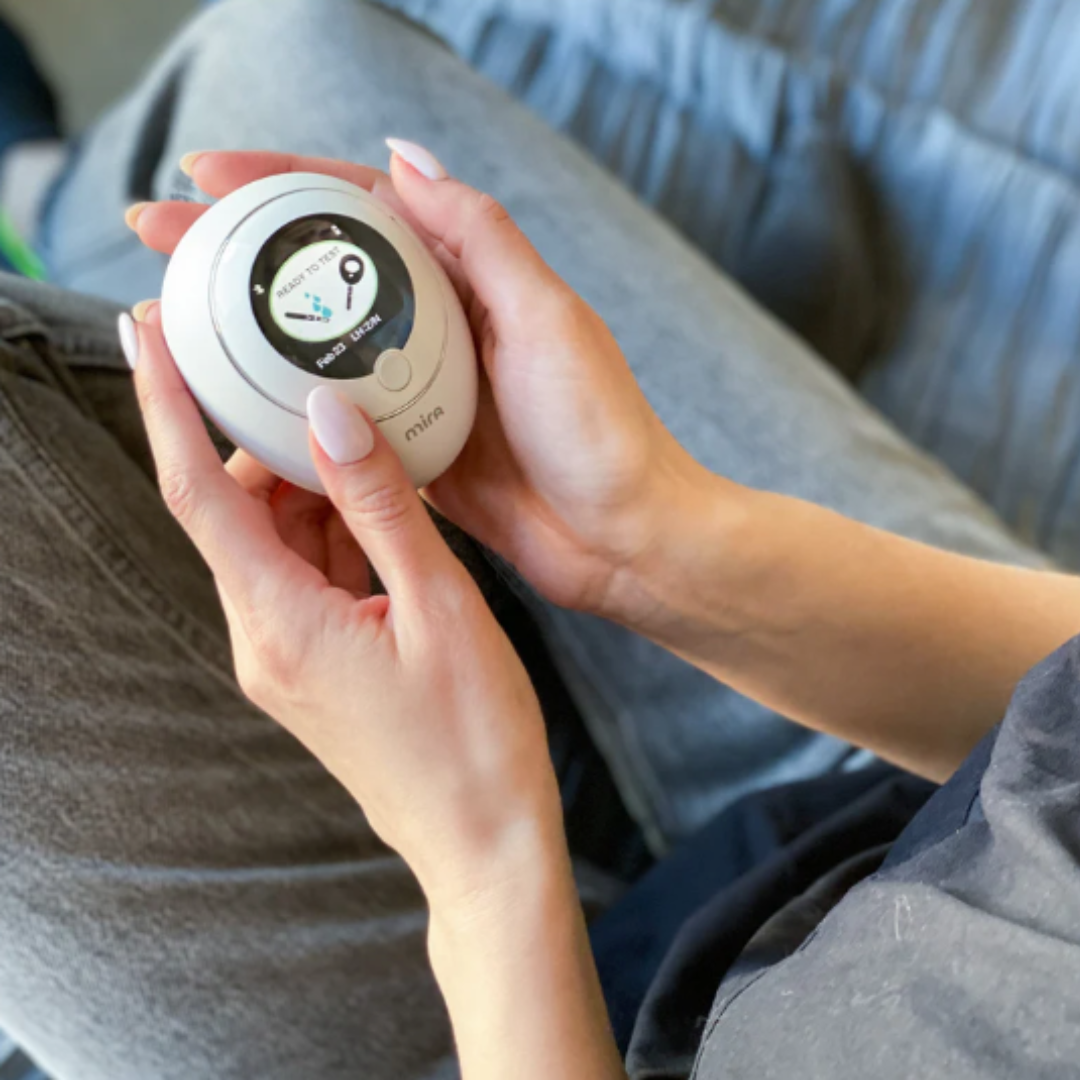 A person holding a white blood glucose meter displaying a blood sugar reading.