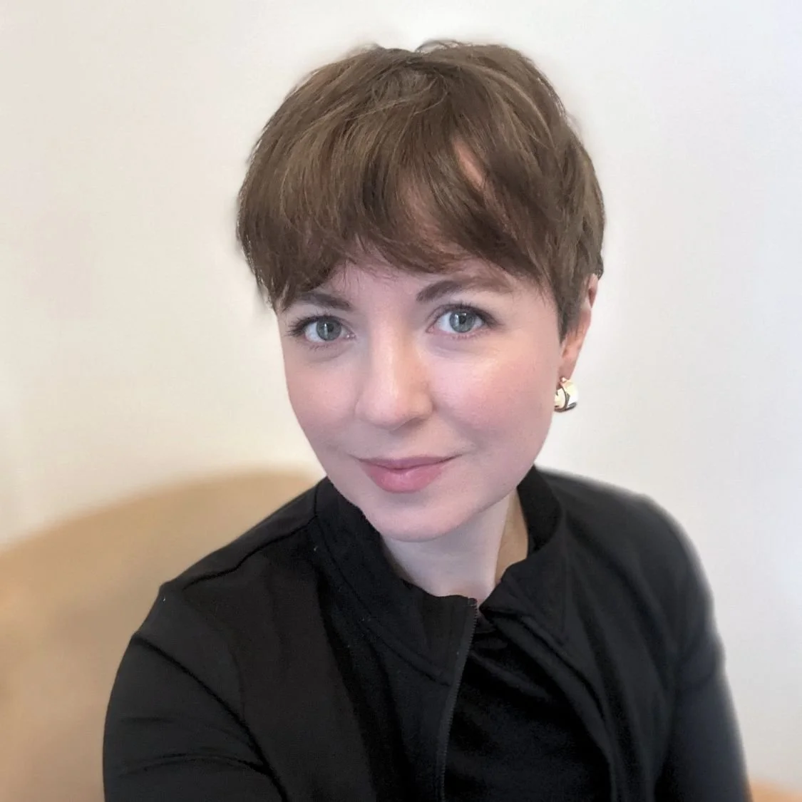 Portrait of a person with short brown hair, wearing a black top and earrings, smiling.