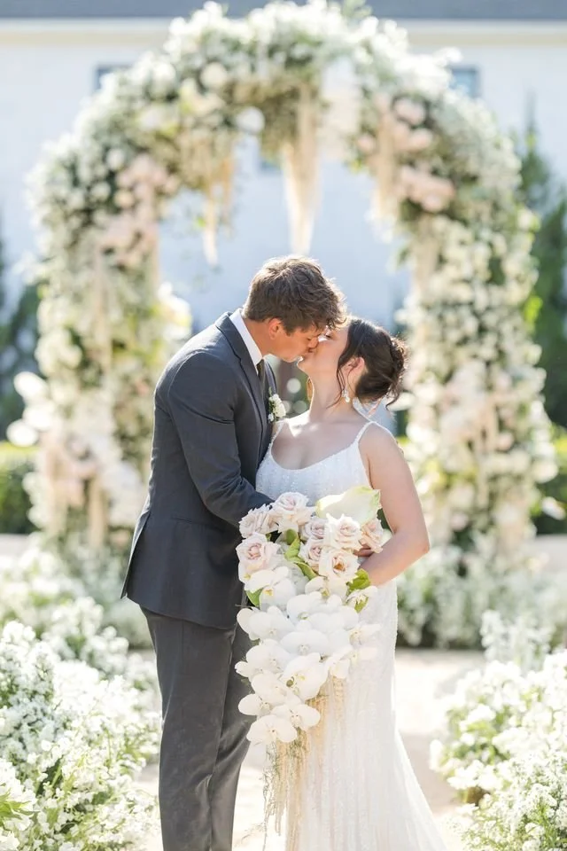 Romantic wedding ceremony featuring a bride and groom under a lush white floral arch with orchids and roses, designed by a New Jersey florist