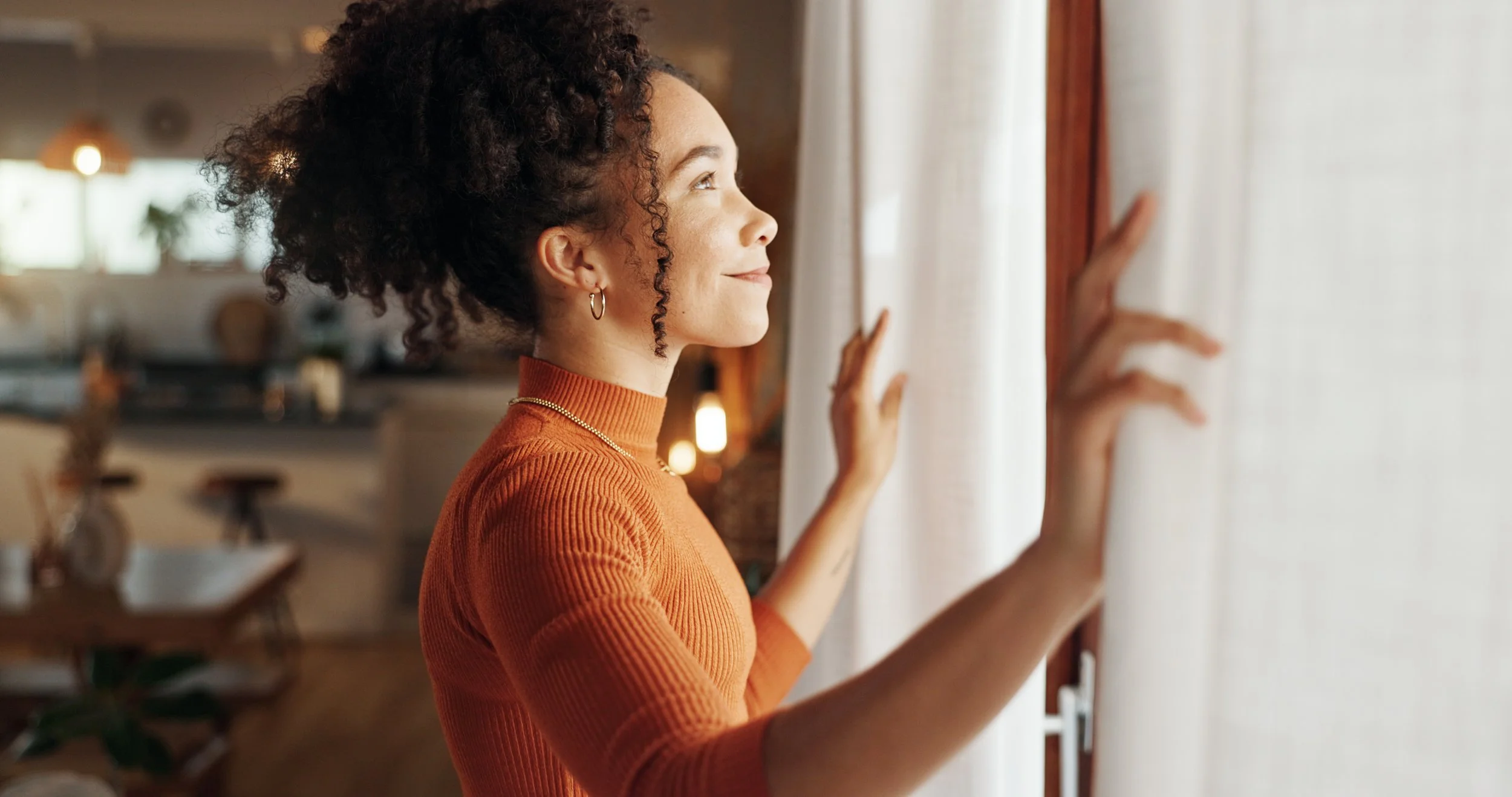 Woman with a soft smile looking out a window in natural light.