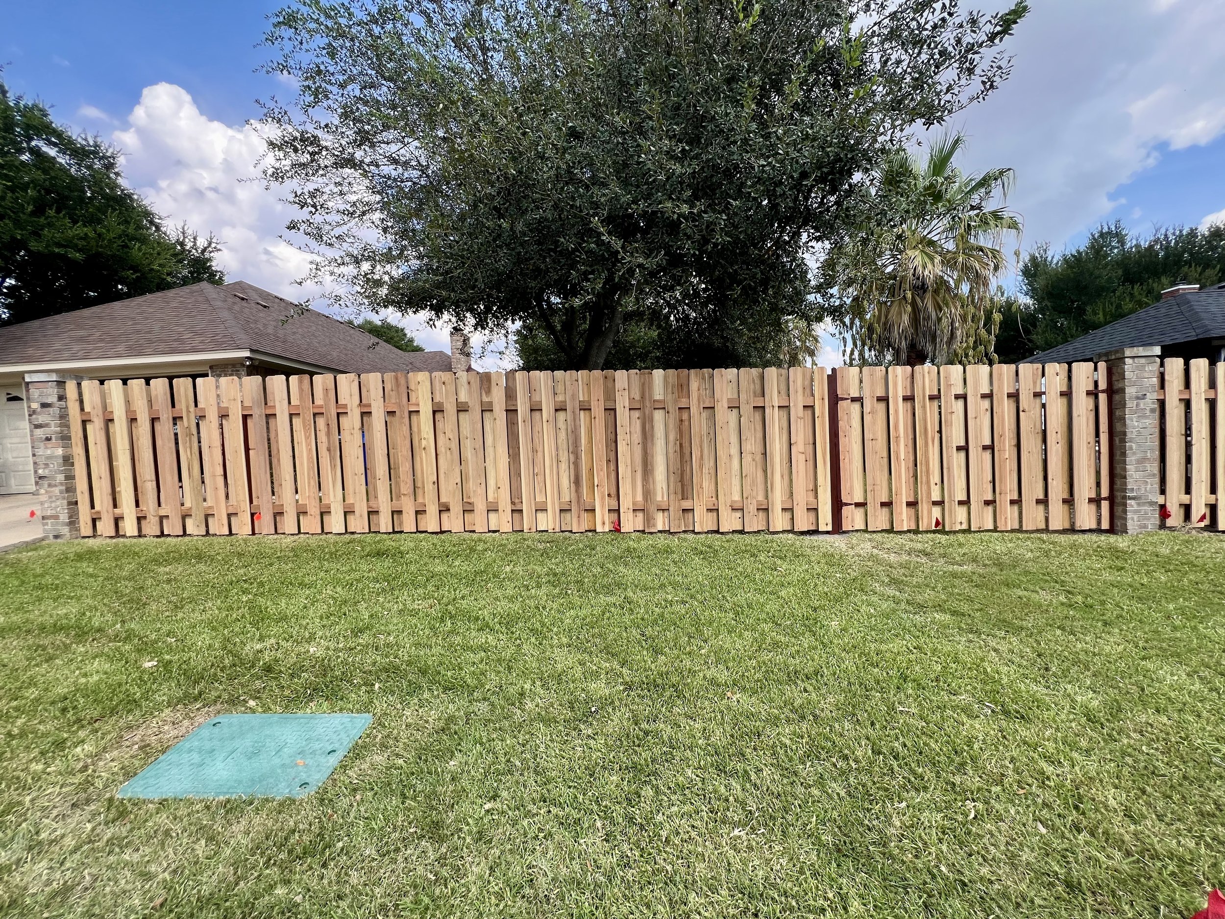 Backyard with a wooden fence, lush green grass, and trees under a partly cloudy sky.