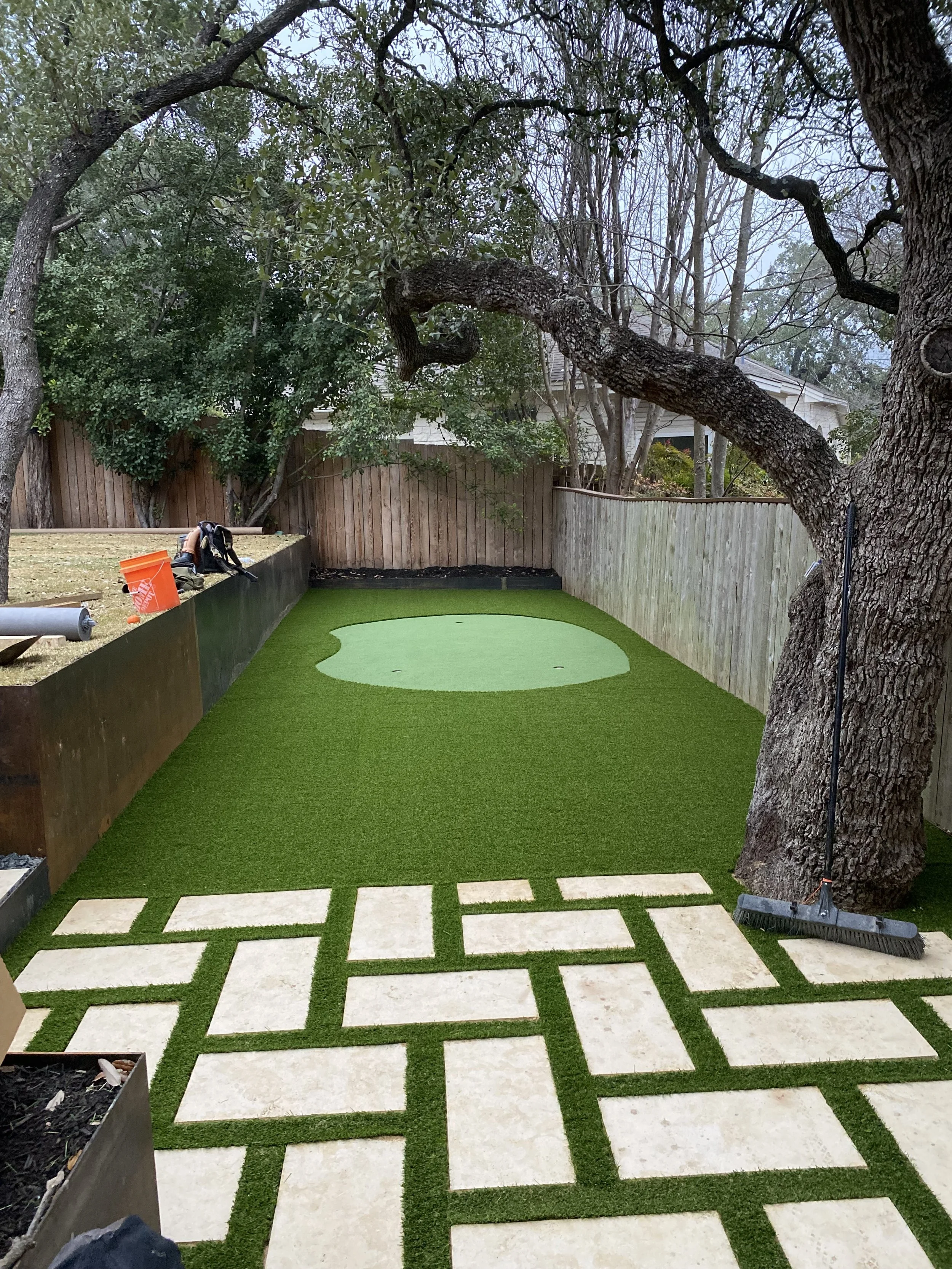 Backyard mini golf course with artificial turf, decorative pathways, a tree, and a small putting green in the corner.