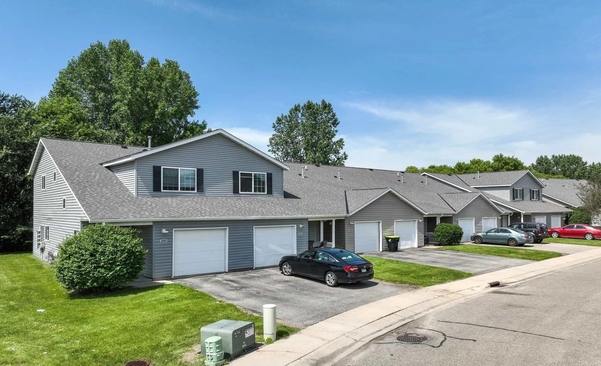 A row of modern gray townhouses with garages and cars, like stylish apartments in Rochester, on a sunny day.