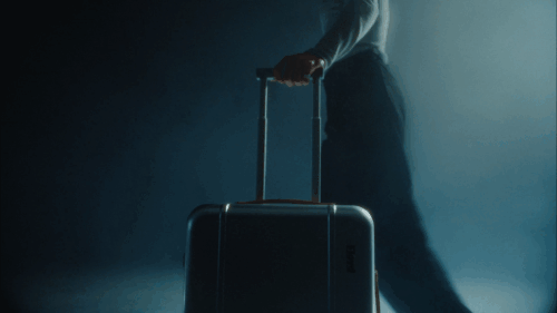 Person mit Trolley-Koffer in einem dunklen, nebligen Raum.