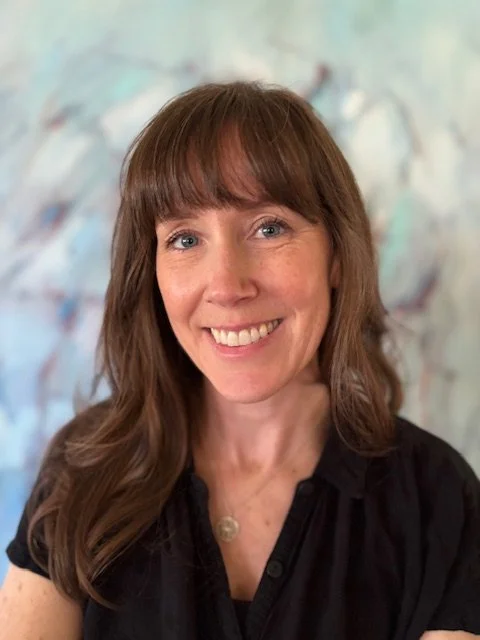 photo of executive director krista palmer, with a black shirt standing against a blue painting background