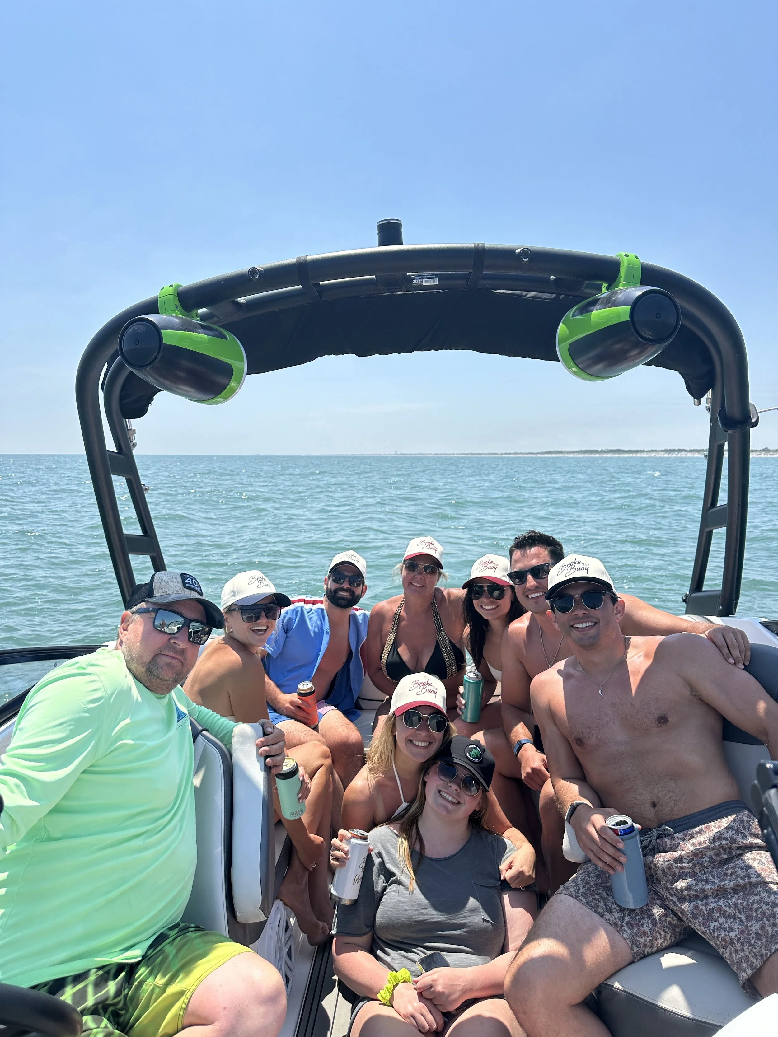 Group of friends on a boat enjoying a sunny day on the water with clear blue sky and ocean in the background.