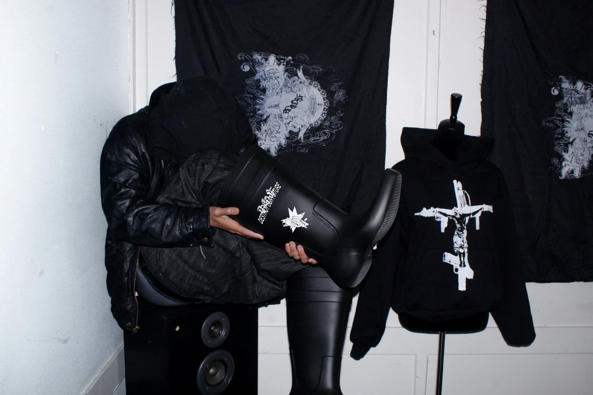 Person in black leather jacket holding a black hairdryer with white text in a room decorated with black banners featuring white graphic designs.