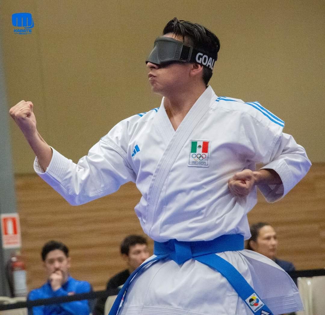 Persona practicando karate con un antifaz y uniforme blanco, cinturón azul, en un entorno de competición.