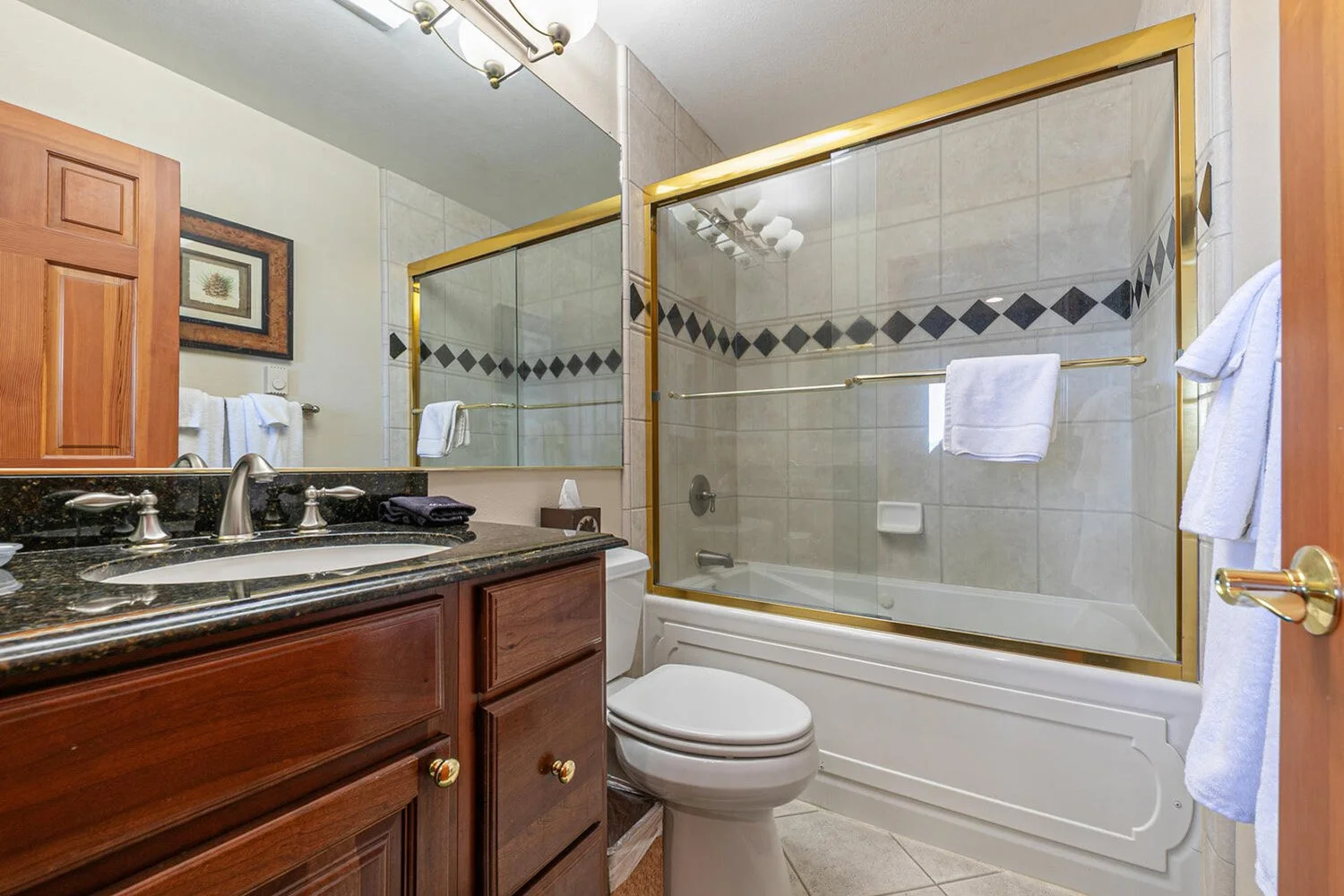 unit 42 main bathroom with tiled shower with glass doors, dark wood cabinets and dark granite counter