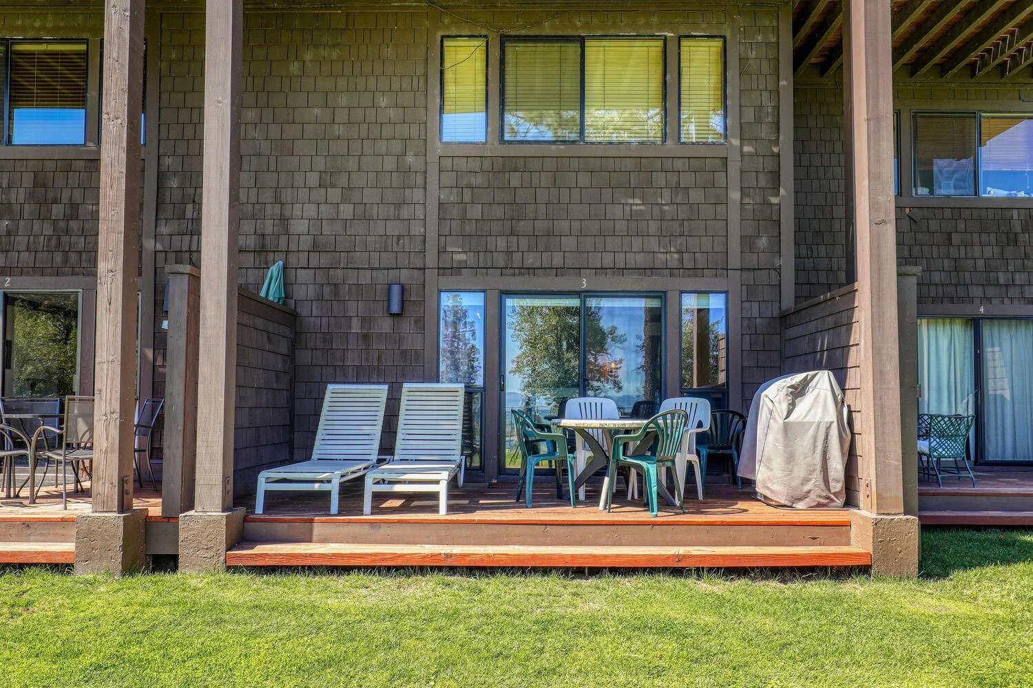 unit 3 back patio as seen from the lawn. shows lounge chairs, table, and grill