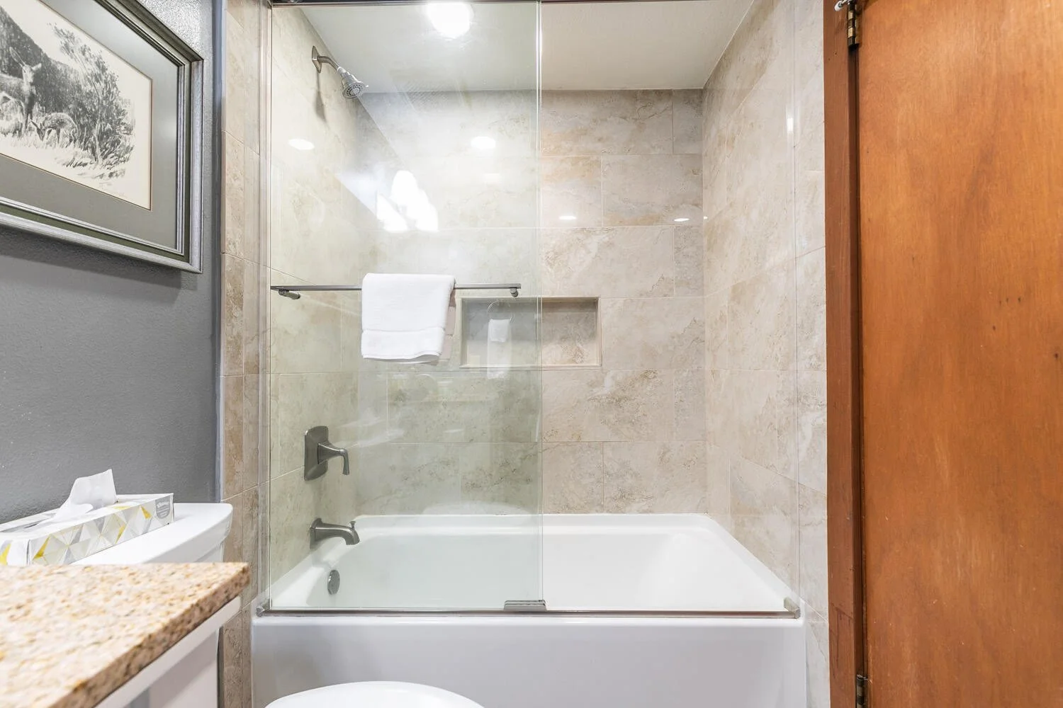 unit 2 view of bathtub/shower combo. beige marble and glass shower doors