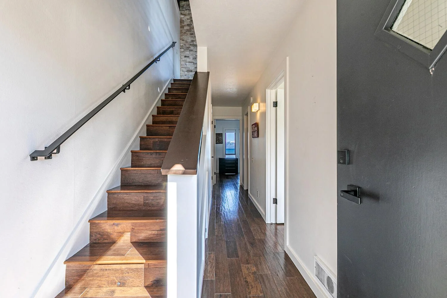 inside front door showing dark wood stairs, white hallway with living room at far end
