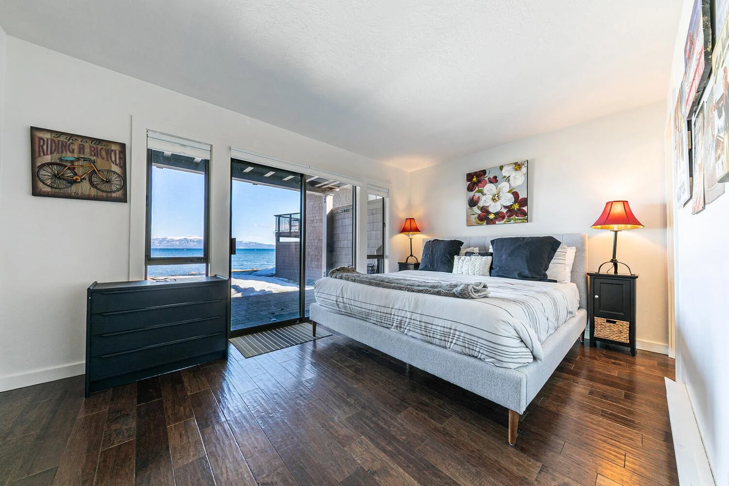 main bedroom with light gray padded platform bed, dark furniture, view of lake through sliding doors