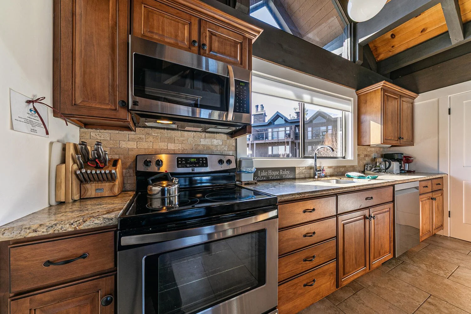 unit 41 kitchen showing stainless steeel stove and view of other units through window over sink. dark cabinets and granite counters