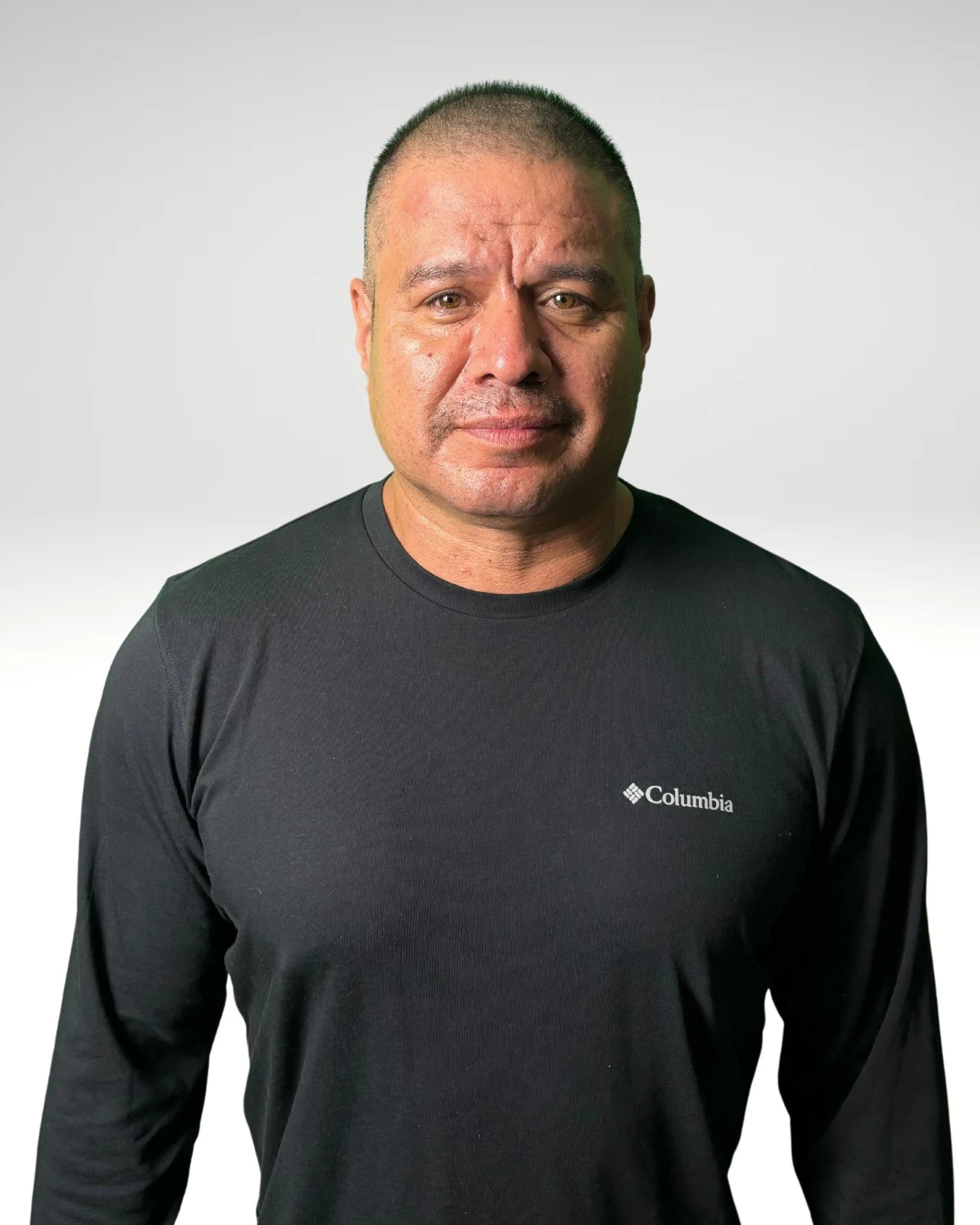 A man with short hair and a serious expression, wearing a black Columbia long-sleeve shirt against a plain white background.