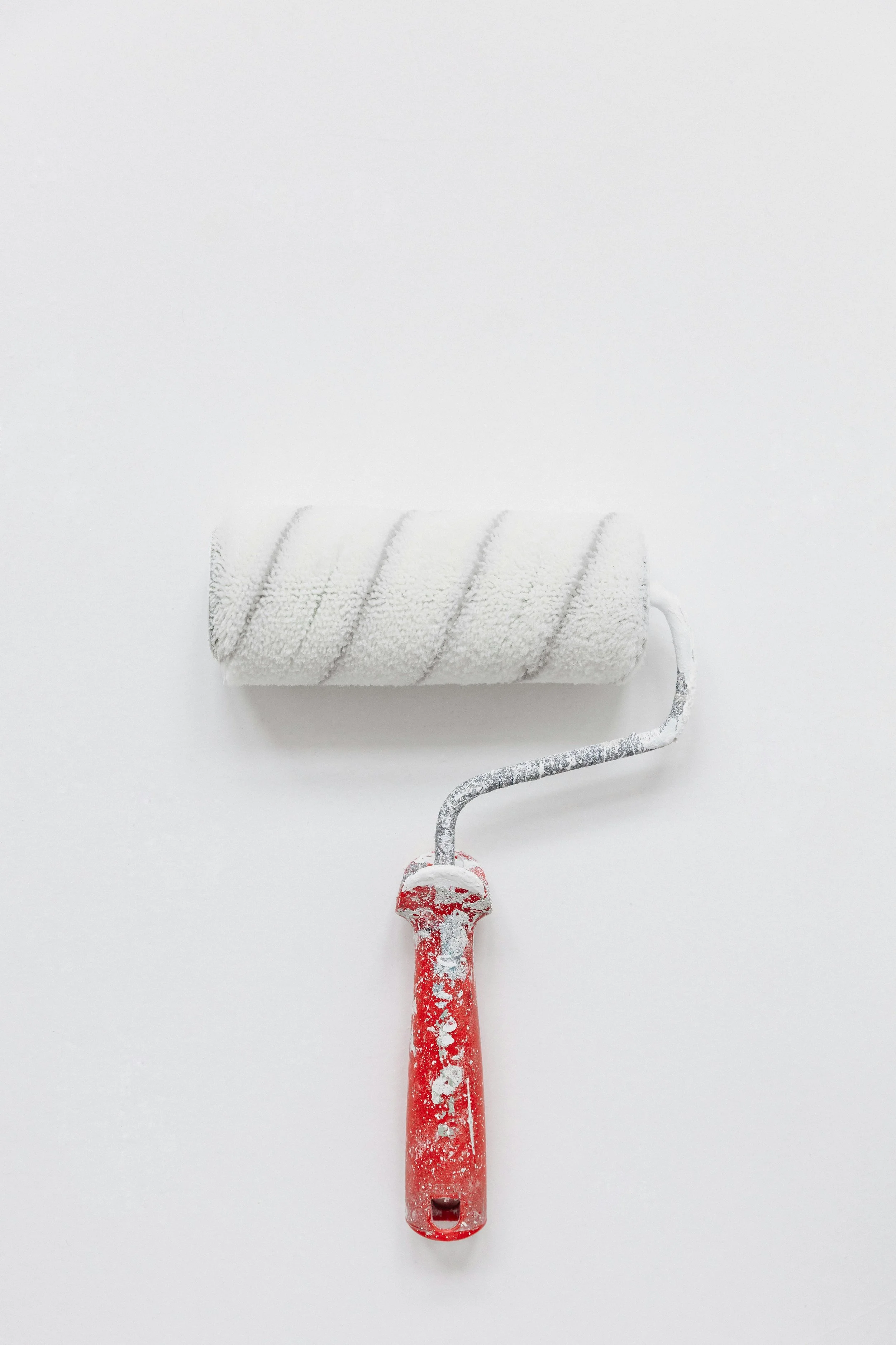 A paint roller with a white fluffy cover and a red handle, covered in white paint, placed on a white surface.