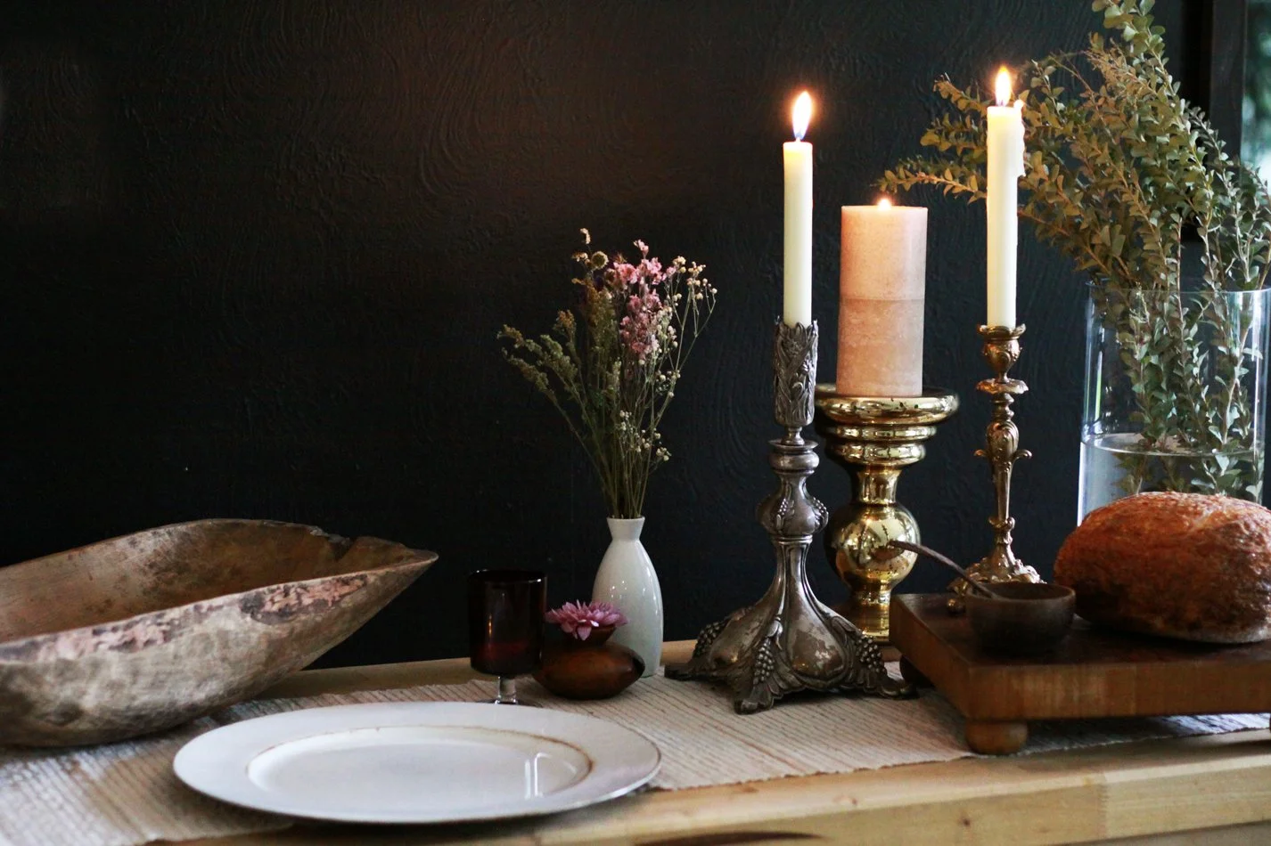 A dining or coffee table decorated with candles, flowers, and a large stone. The background is a dark wall.