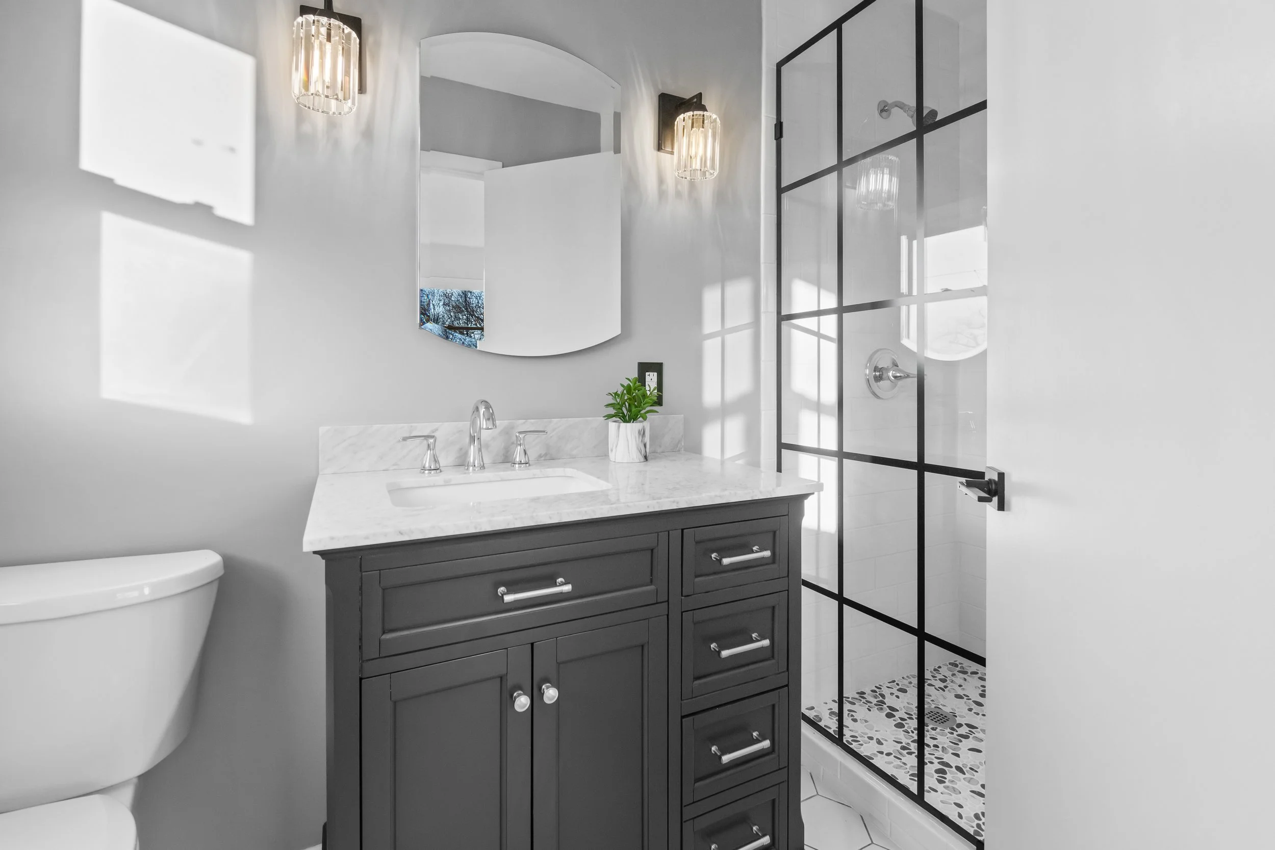 Modern bathroom with a black vanity, white countertop, round mirror, and glass shower with black framing.