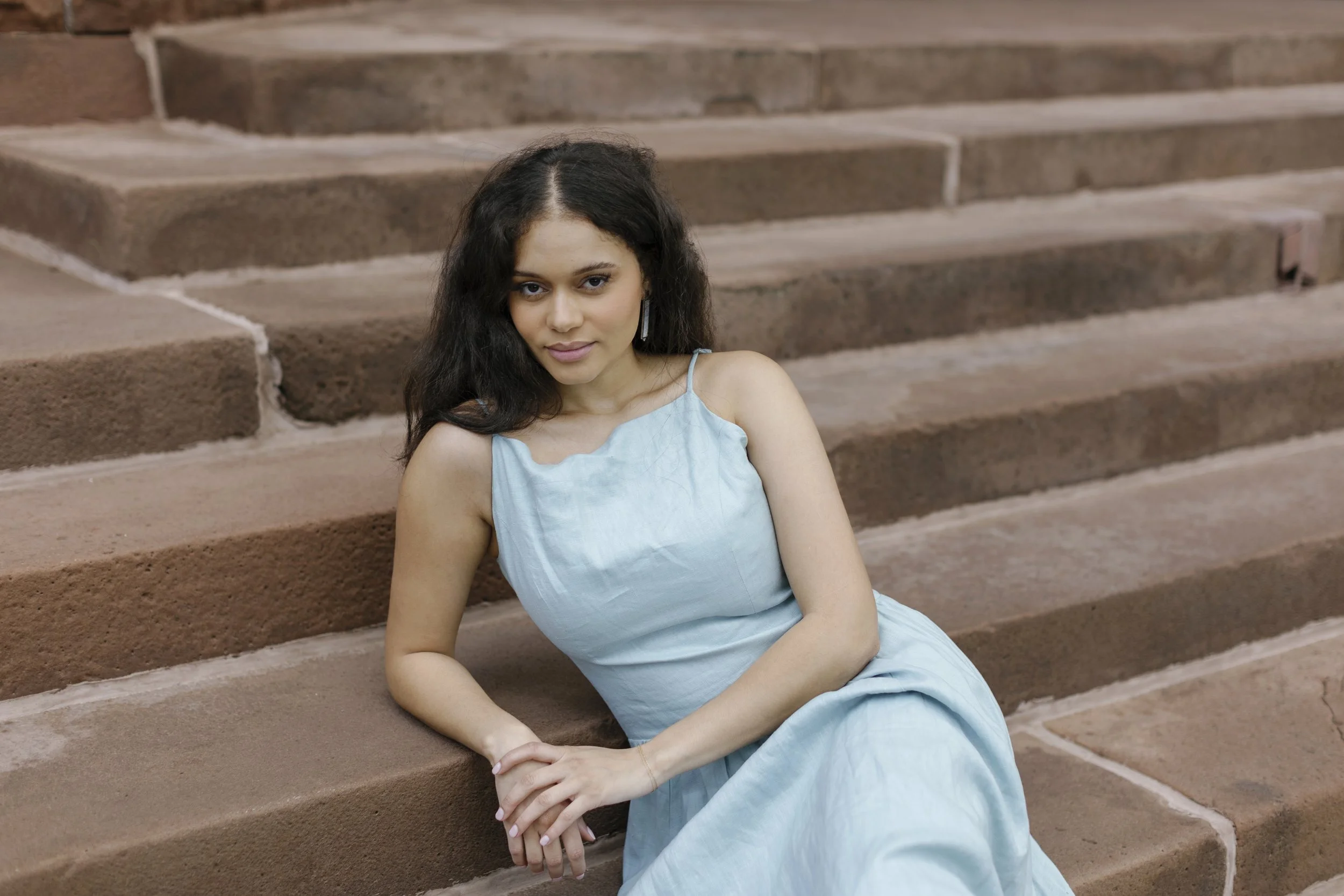Young woman in a light blue dress sitting on outdoor stone steps.