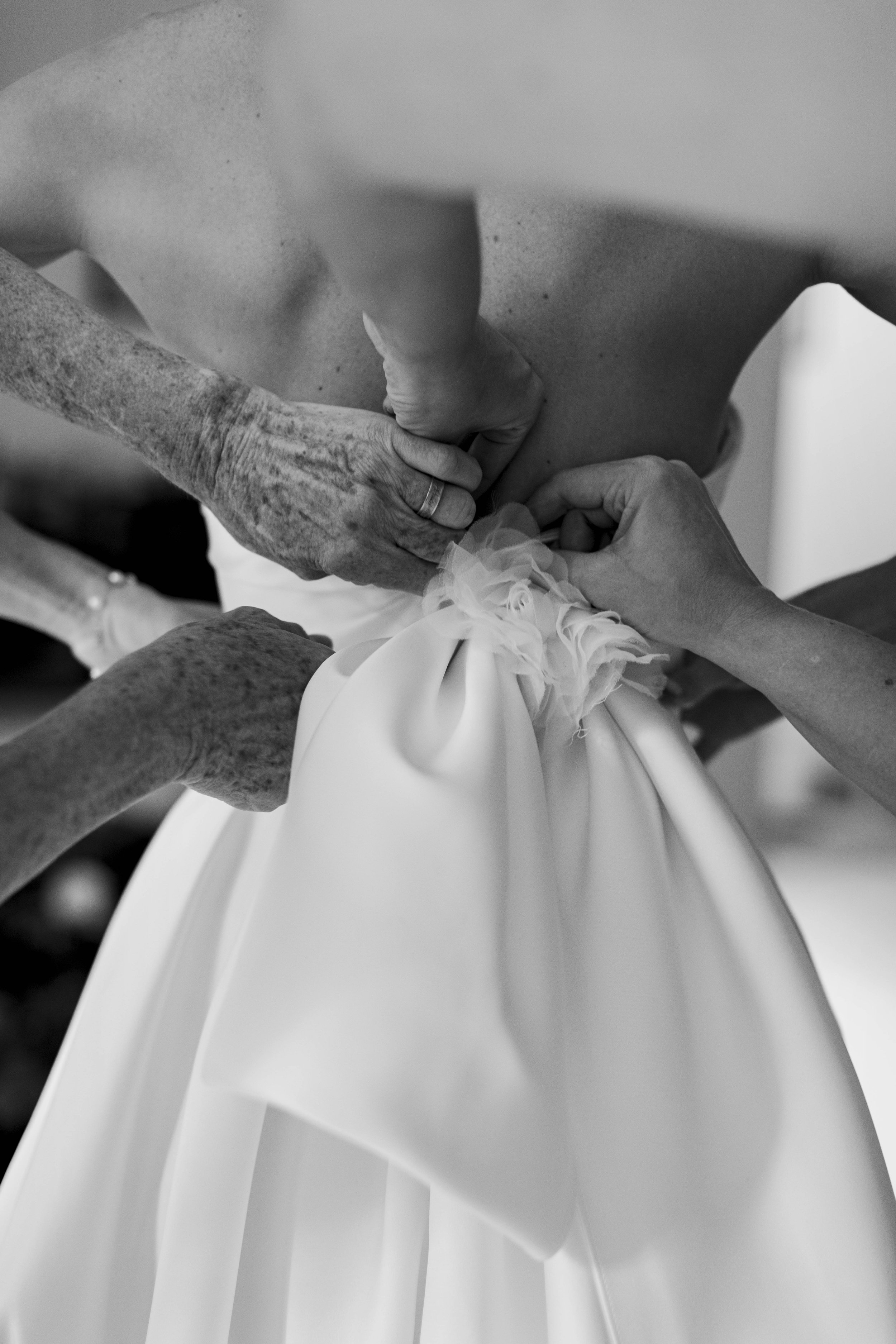 Close-up of hands fastening a wedding gown, back view.