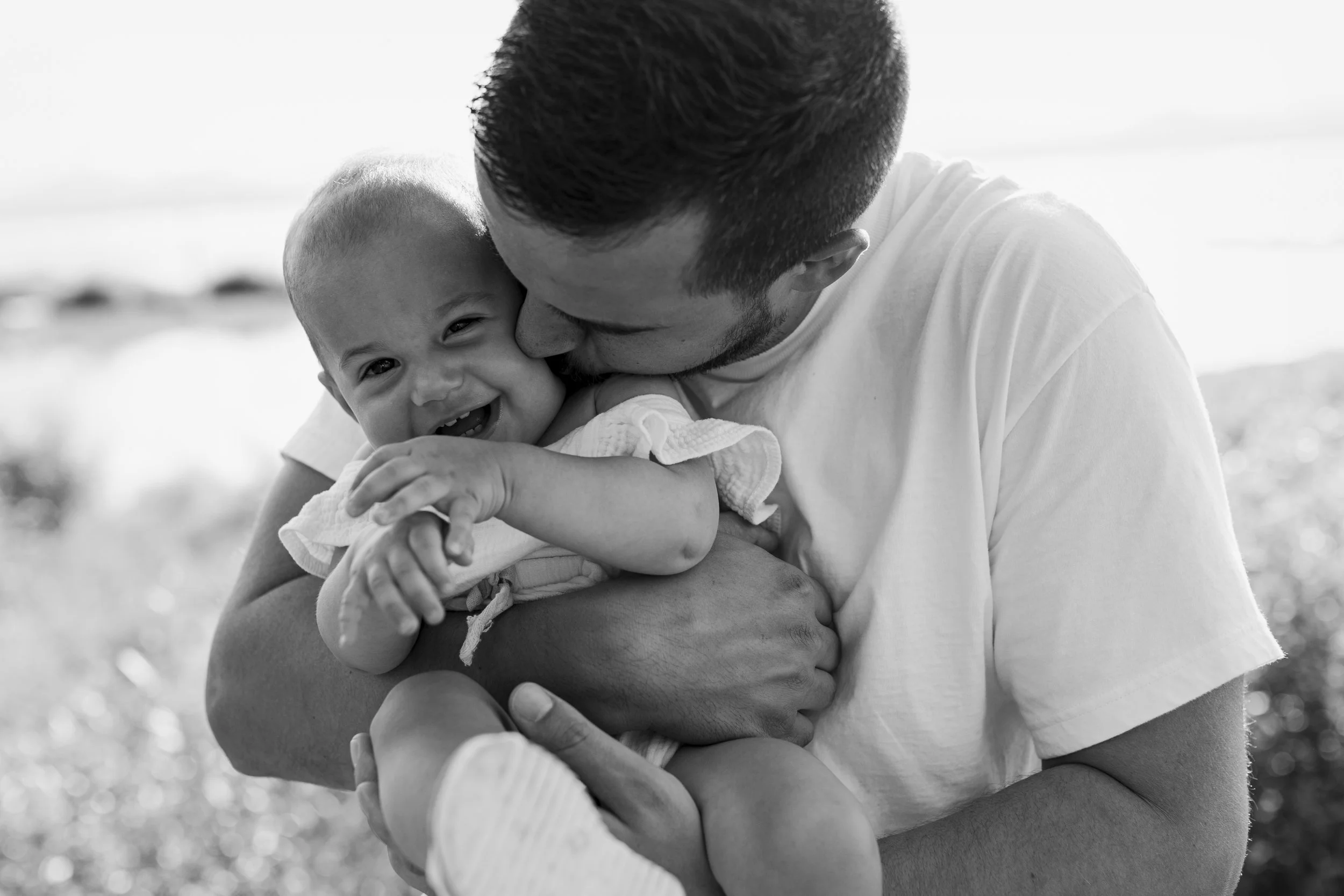 A man holding a smiling baby girl outdoors, sharing a tender moment.