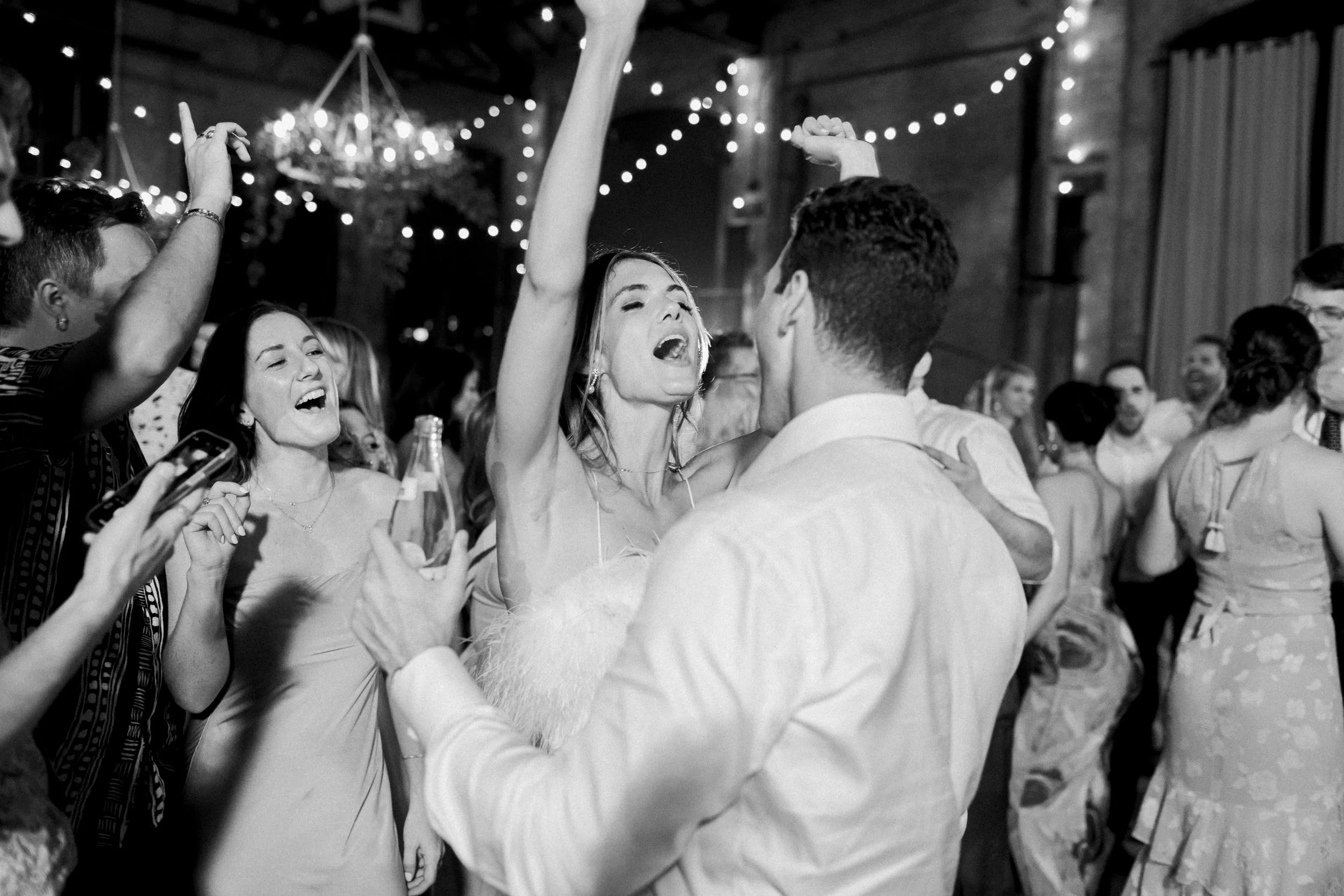 People dancing and celebrating at an indoor event with string lights.