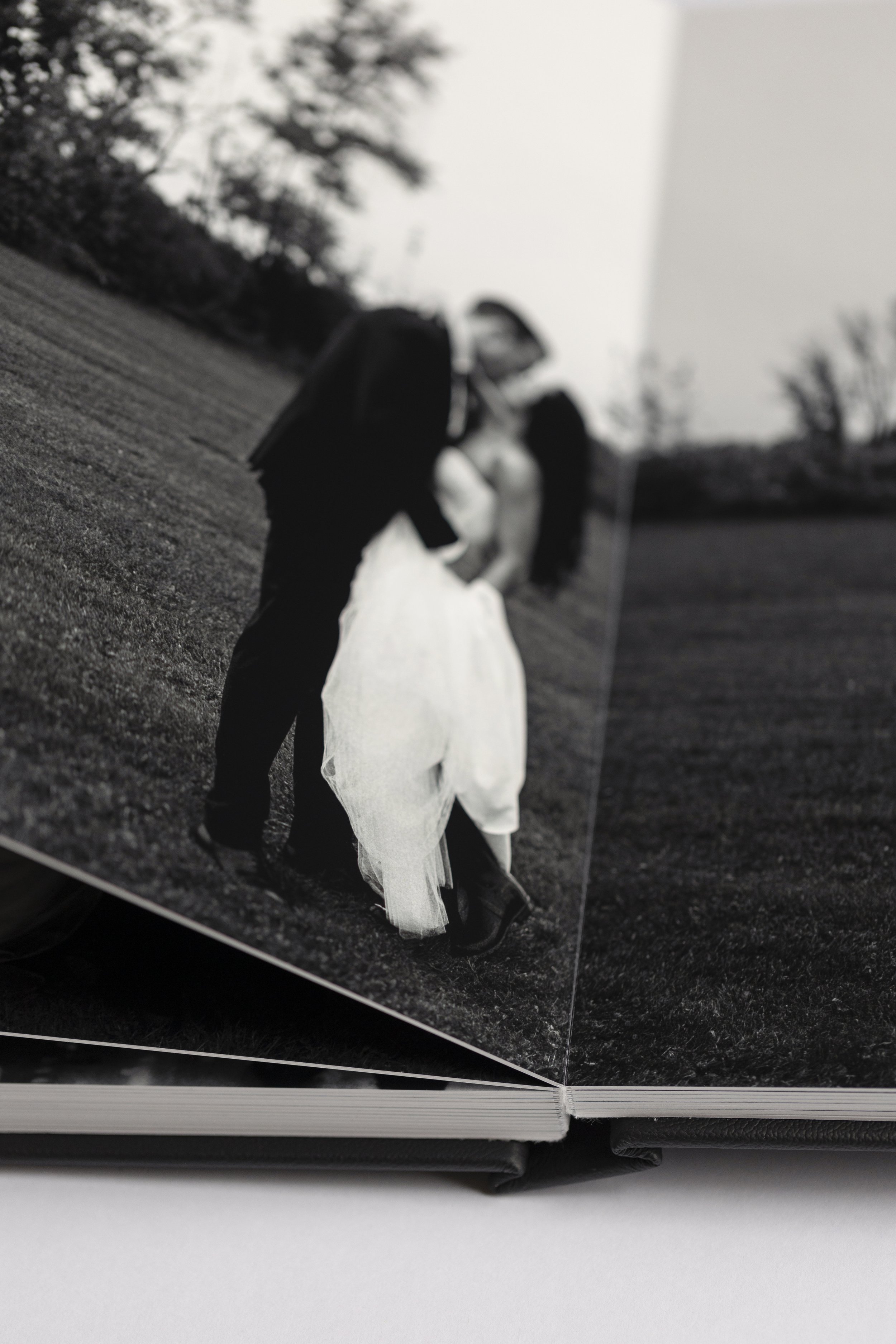 Black and white photo of a wedding album page, showing a bride and groom kissing in a grassy outdoor setting.