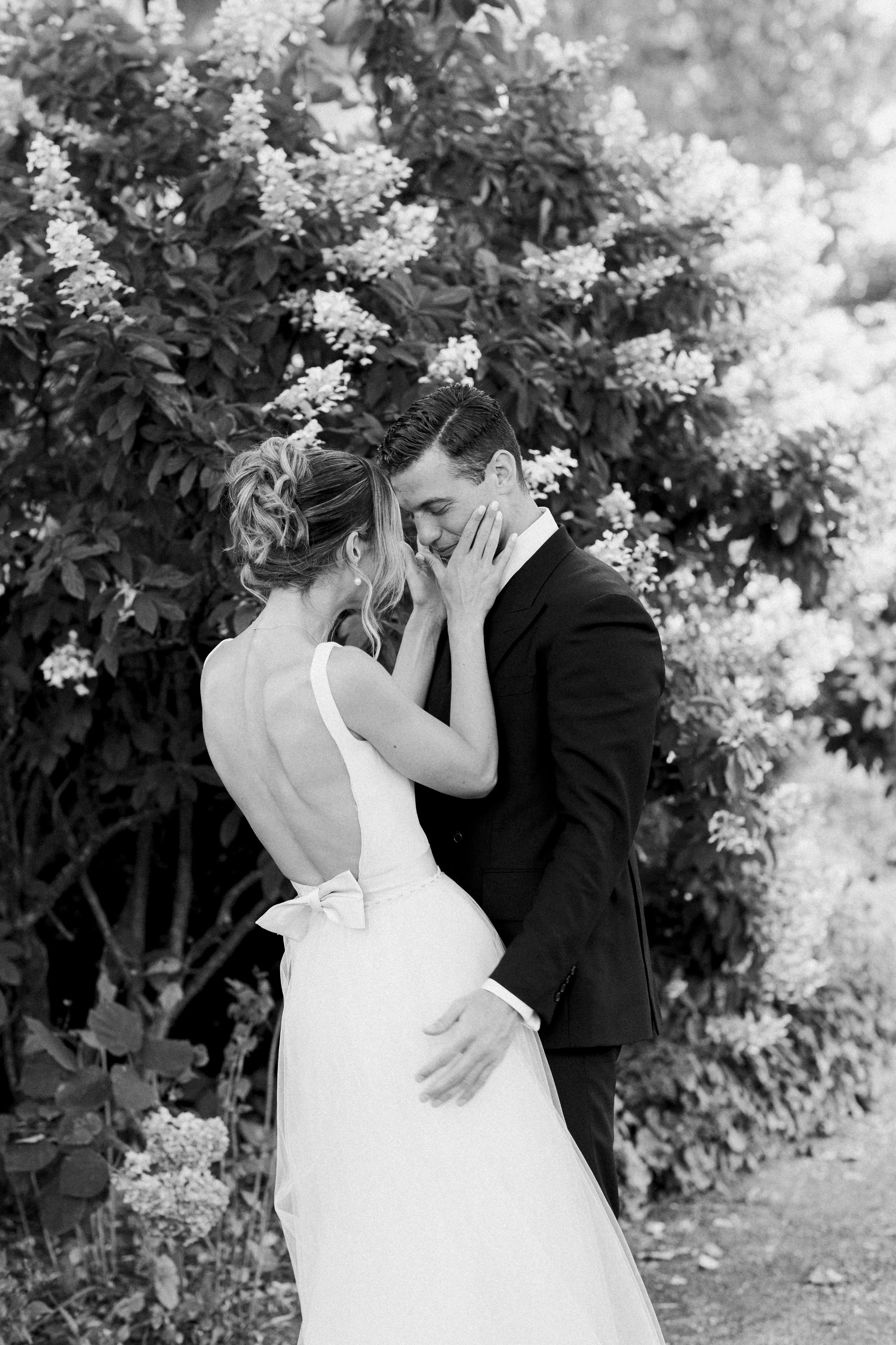 Bride and groom embracing in a garden setting with flowers.