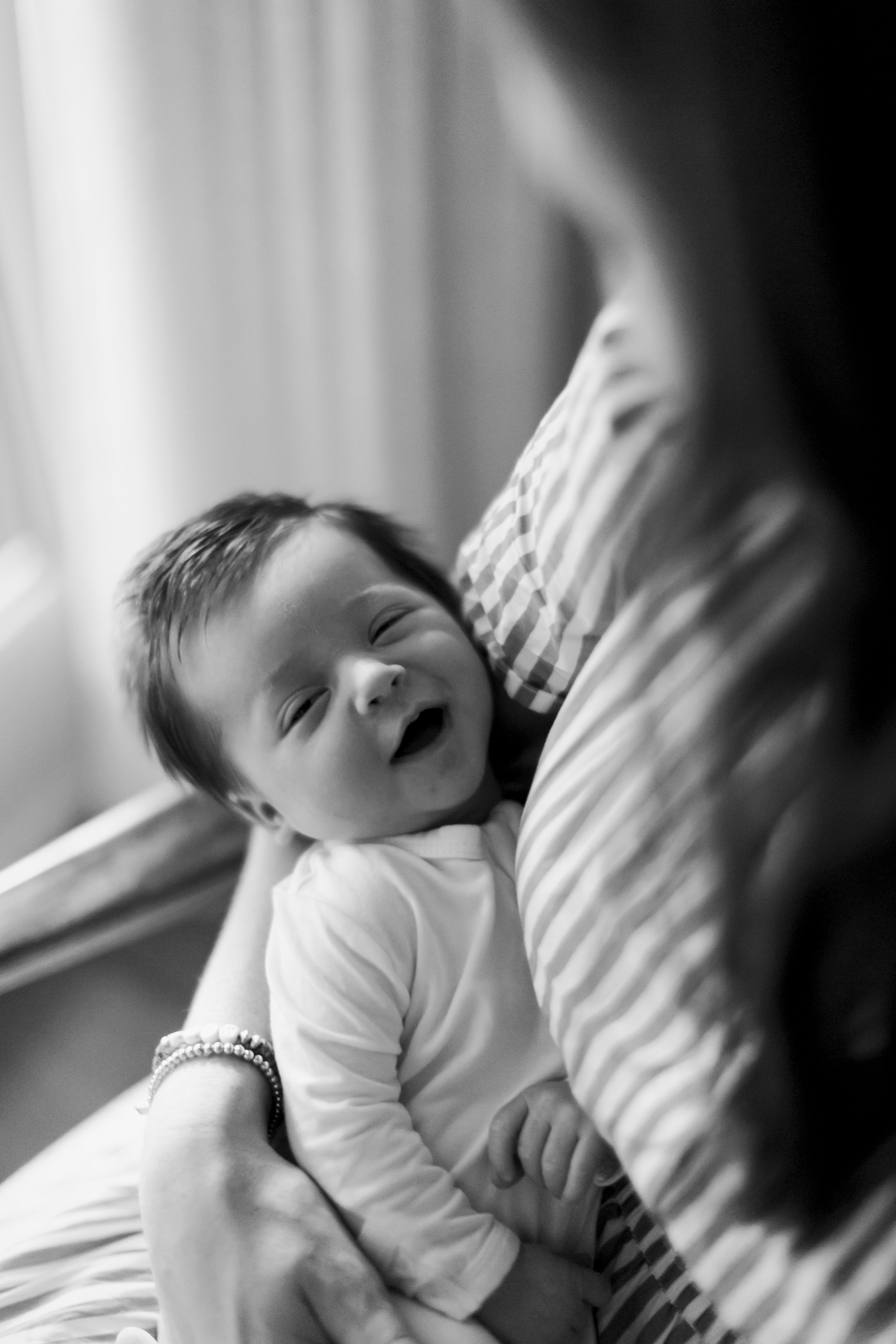 A smiling toddler being held by a woman, possibly his mother, in a cozy, softly lit room.