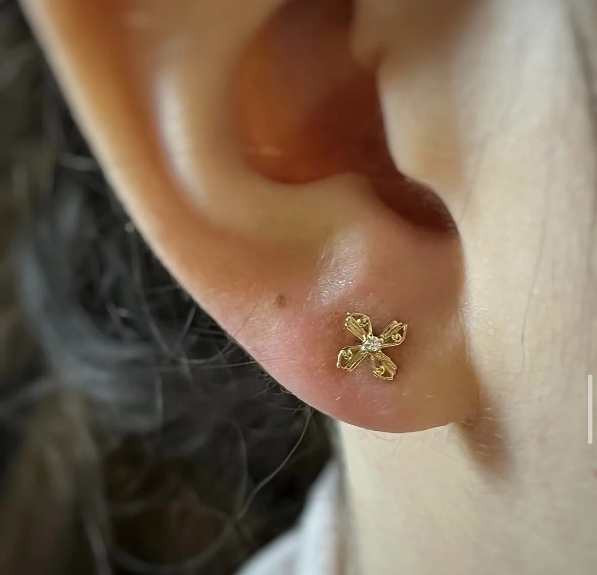 Close-up of a person's ear wearing a gold flower-shaped earring with a small gemstone in the center.