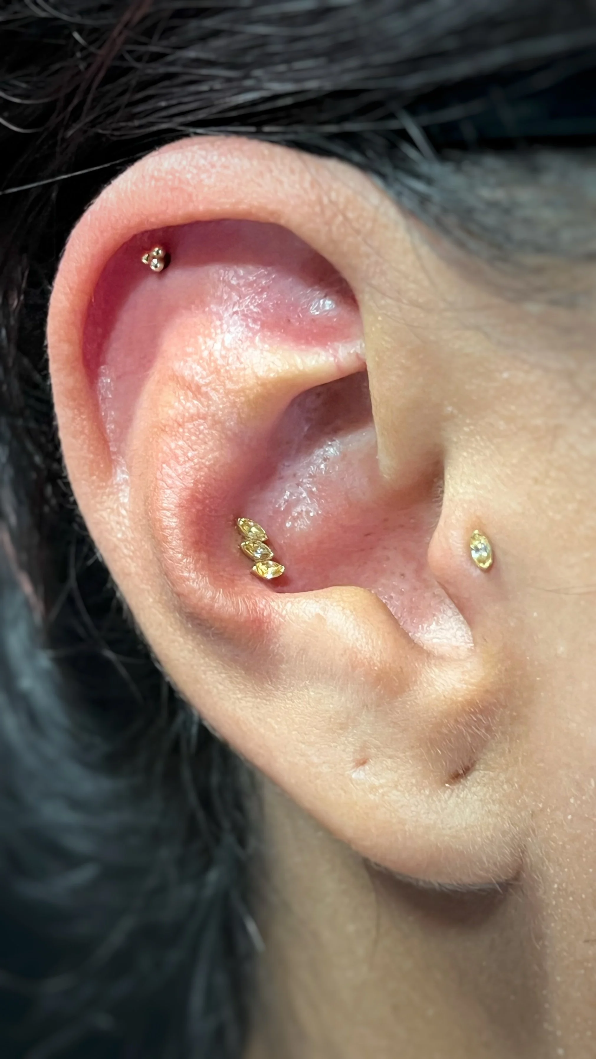 Close-up of a person's ear with multiple gold and diamond earrings.