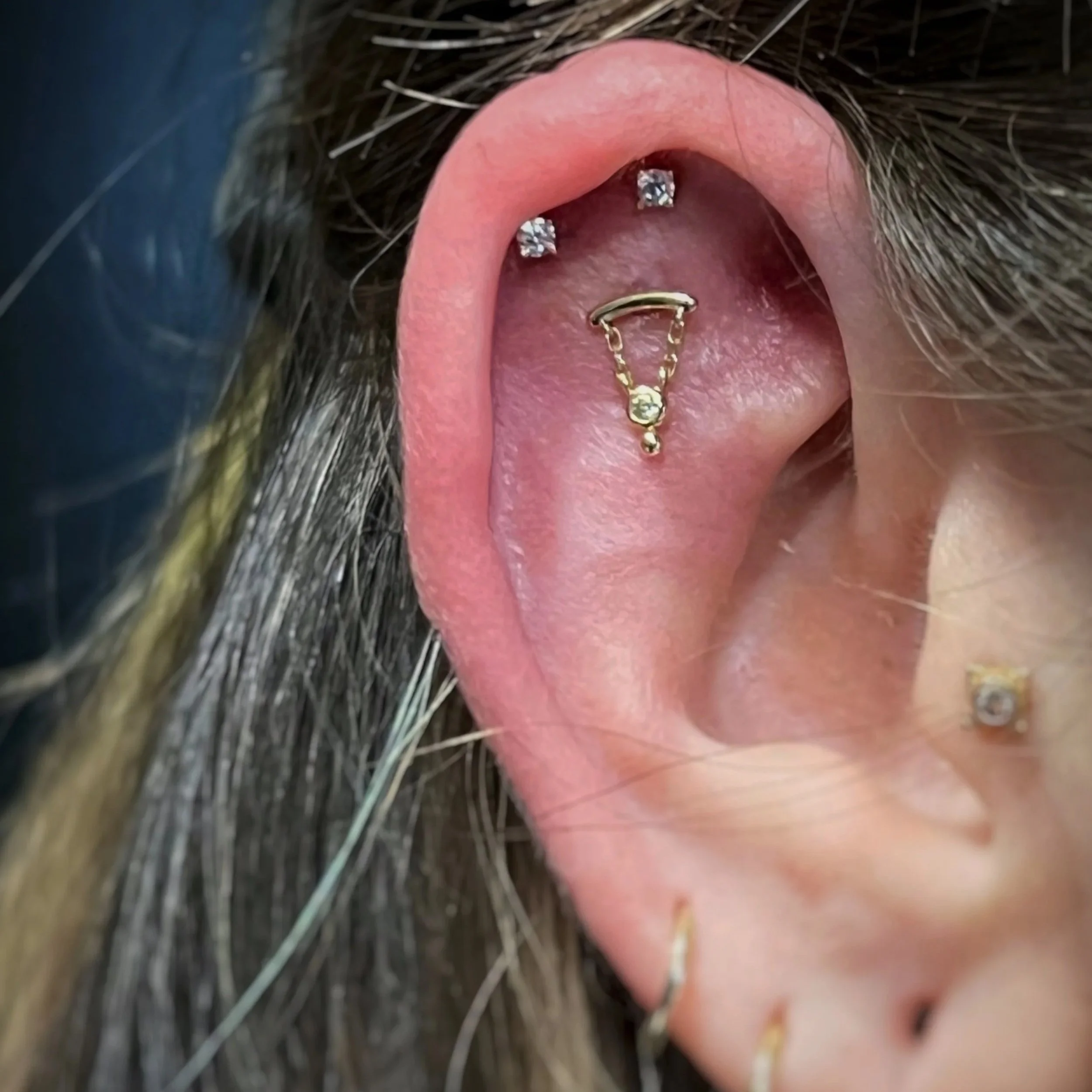 Close-up of a person's ear with multiple piercings, including two diamond stud earrings above a gold dangly earring