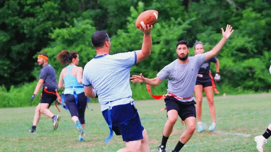 Group of people playing flag football outdoors on grass field in a Charlotte NC adult league game.
