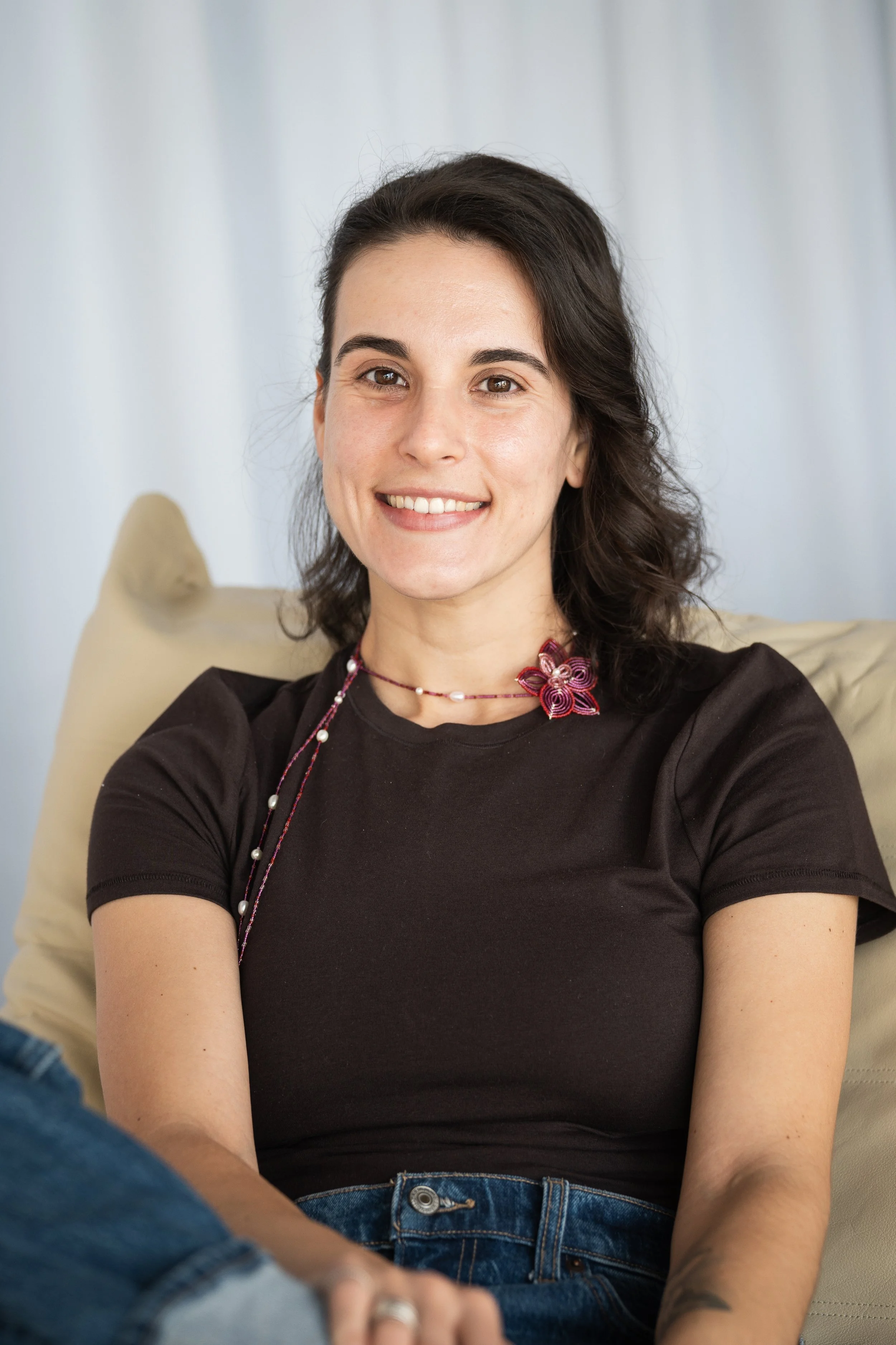 Person sitting on a chair wearing a white shirt, blue jeans, and a colorful striped shawl, against a plain background.