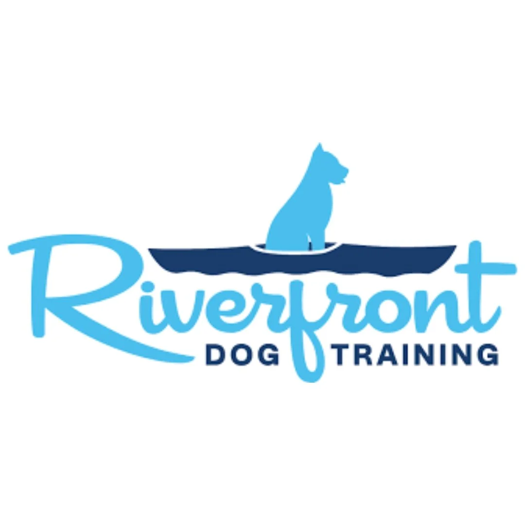 Logo for Riverfront Dog Training featuring a blue dog silhouette sitting in a stylized boat above the text 'Riverfront Dog Training' in blue and navy lettering.