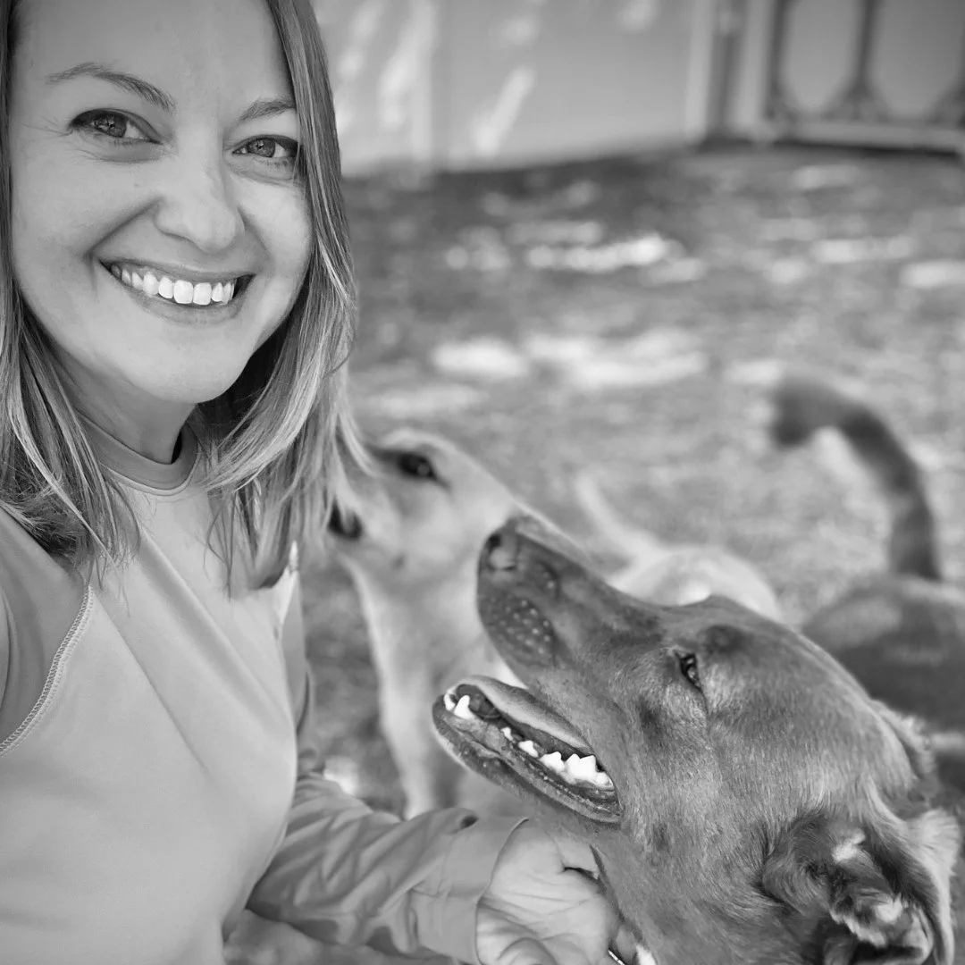 A woman smiling and taking a selfie with three dogs outdoors in black and white.